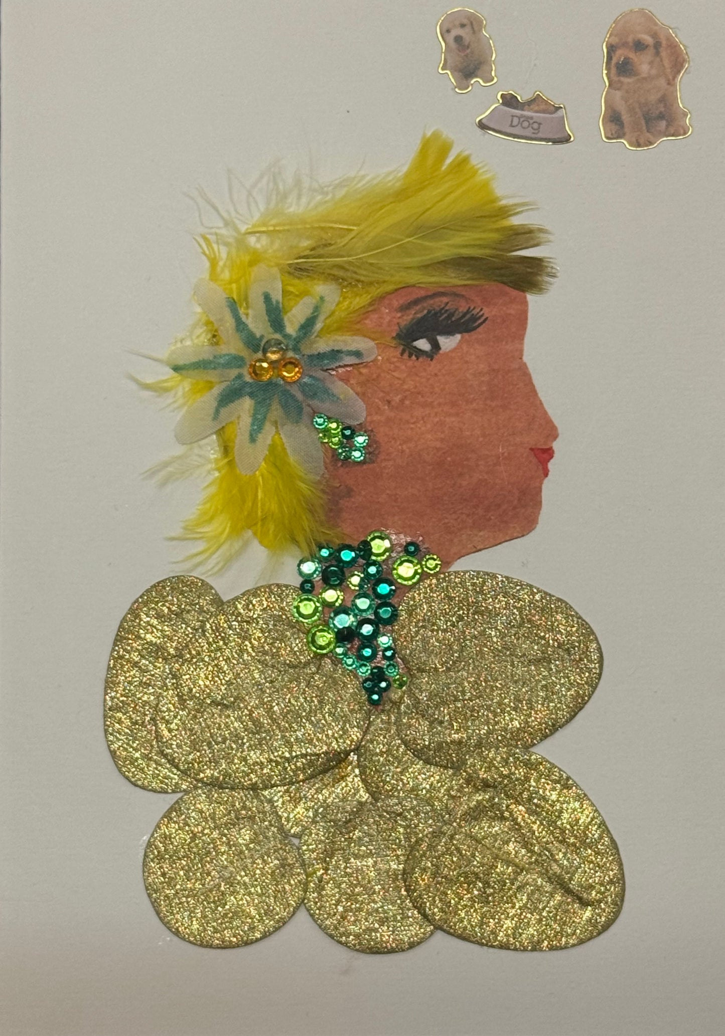 Handmade greeting card that doubles as a piece of art featuring a side-profile silhouette of a woman with a warm complexion. Her hair is styled with bright yellow feathers that fan outward, creating a soft, textured halo around her head, accented by a multicolored floral embellishment placed near her ear. She wears green gem jewellery for neckalce and earrings. Her top is glittery gold, that is made up of circle shapes. Placed in the top right corner is three dog stickers above her head that add character.