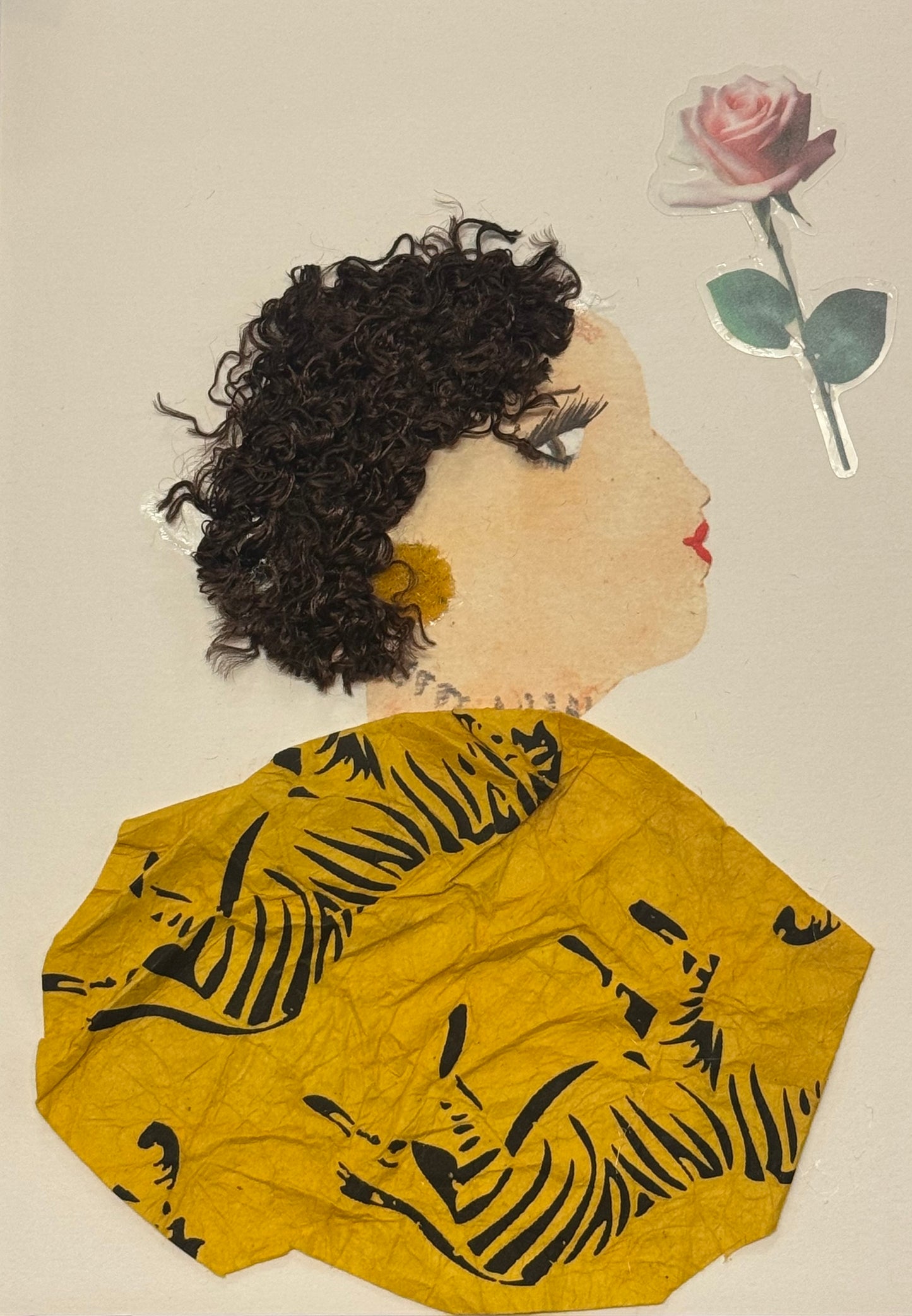 Handmade greeting card that can double as a piece of art featuring a side-profile portrait of a woman with short, curly dark hair made from textured material, a soft pink rose placed behind her head, and a mustard-yellow patterned garment with black leaf designs. The face is softly painted with delicate lashes and red lips, and the overall composition combines fabric and paper elements to create a warm, elegant, and textured mixed-media design.