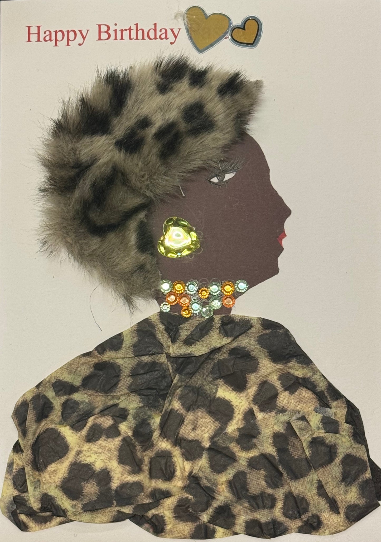 Handmade greeting card that can double as a piece of art featuring a side-profile silhouette of a woman with a deep brown complexion wearing a textured leopard print outfit and a fluffy faux fur hat with black and tan spots. She is adorned with a large gold gem earring, a multi-colored rhinestone choker necklace, and small facial details including long lashes and red lips. The top of the card reads “Happy Birthday” in soft red lettering with two gold hearts beside it, all set on a clean white background.