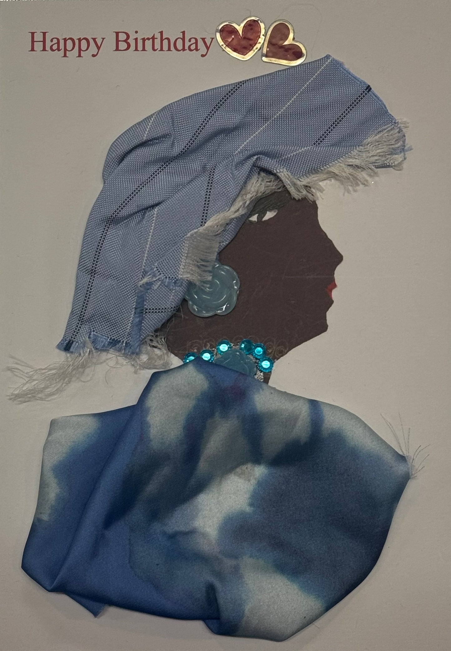 Handmade birthday card that can double as a piece of art featuring a woman wearing a blue headscarf and blue patterned outfit with a sparkling necklace. Two red heart decorations and the words “Happy Birthday” appear above the design.