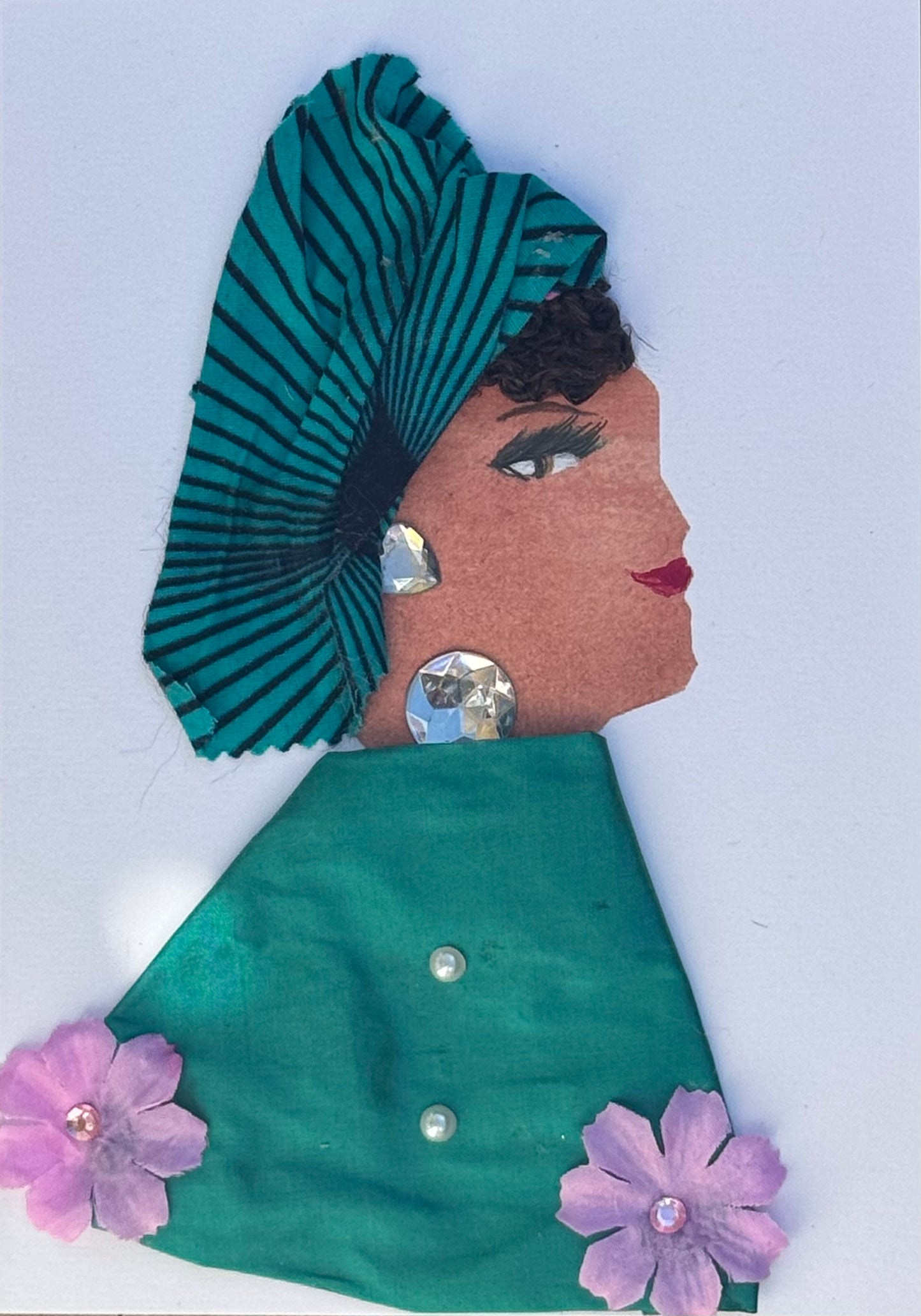 Handmade greeting card that can double as a piece of art featuring a womans side profile who is wearing a teal headwrap with black line patterns across it. She wears a similar coloured shawl but it is plain green without the partern, also has light purple flowers embroidered at the bottom of each corner. There are also two small pearl details on the shawl down the middle as an accent or acting like buttons. For jewllery she wears large silver gems for a neckalce and earrings.