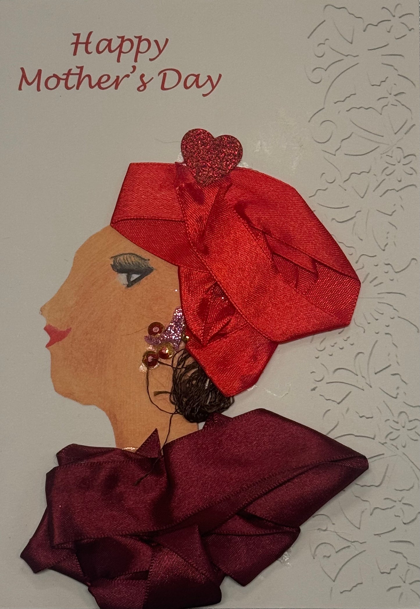 A handmade card titled "Happy Mother's Day" that can also double as a piece of art. It features a profile of a woman wearing a voluminous, pleated red silk headwrap with a red glitter heart on top. She has a large burgundy fabric collar and dangling beaded earrings.