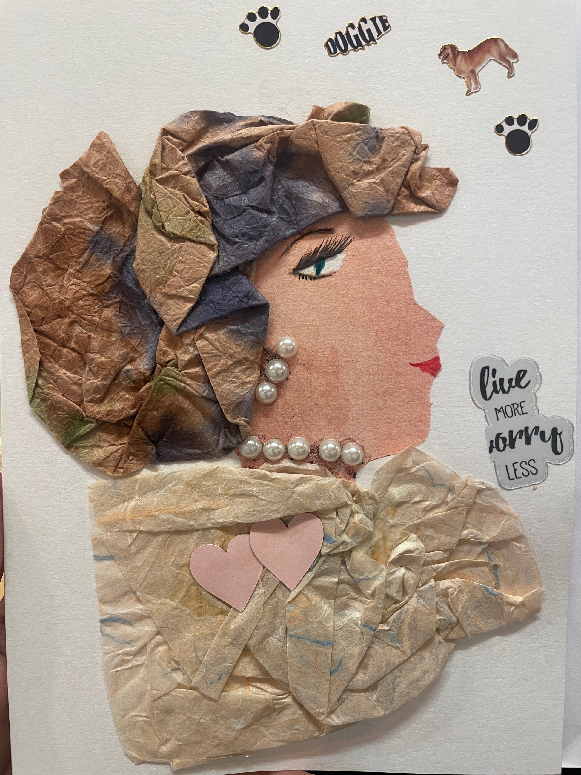 This is a handmade card of a woman named Addison with a crinkled brown and green headwrap, pearl necklace, and a cream tissue-paper outfit. Stickers of hearts, dogs, and paw prints surround her.