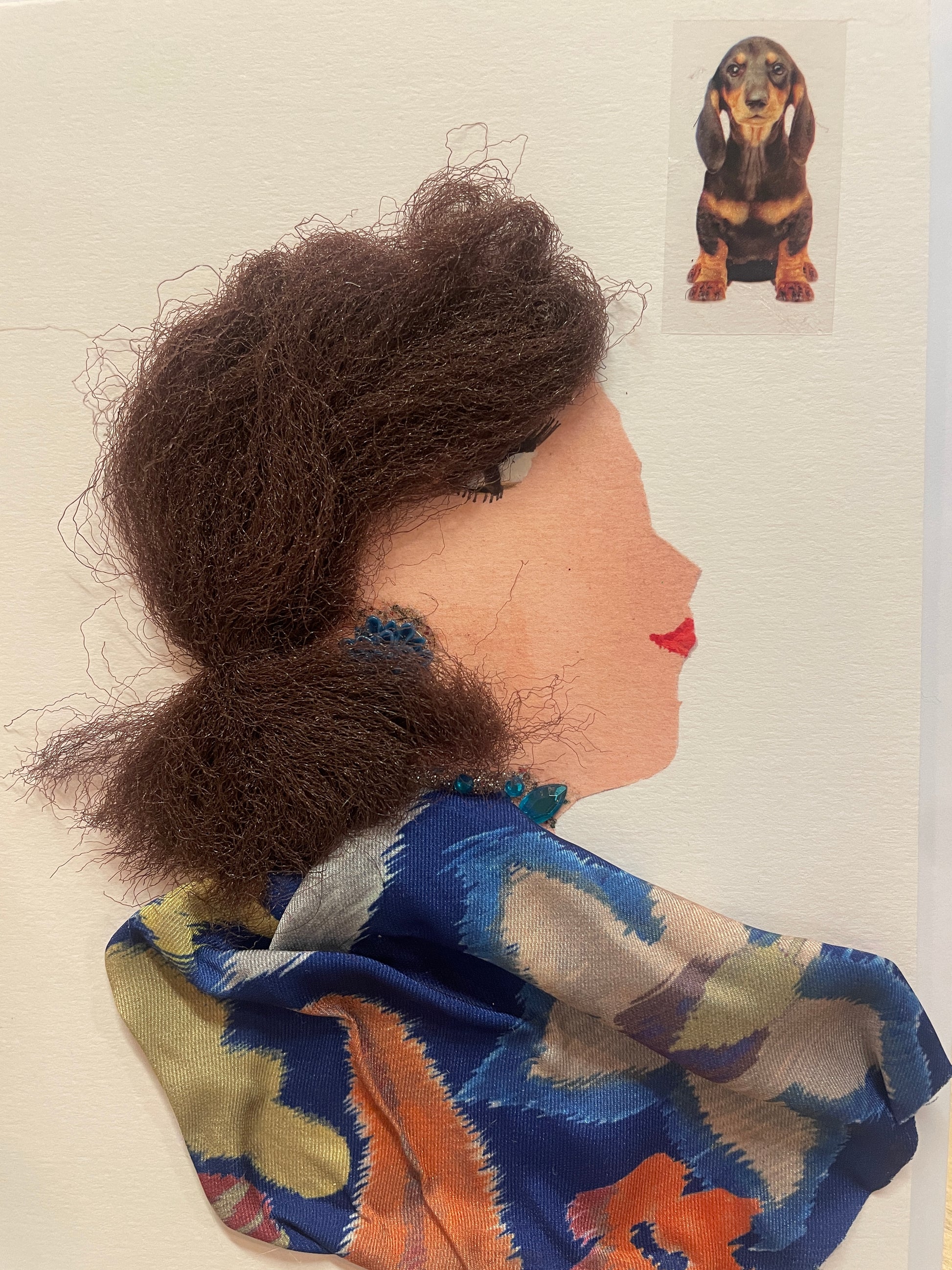 This is a handmade card of a woman named Astonishing Aishwarya, wearing textured brown hair, blue-and-orange floral fabric around her shoulders, and teal beads around her neck. A lovely dog is found in the top right corner.