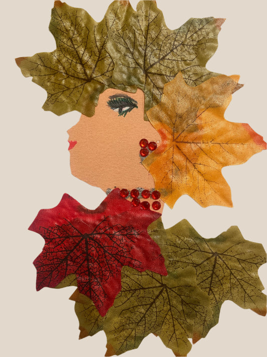 This is a handmade card of a woman named Autumn Aldgate. Her hair and clothing are made entirely of fabric leaves in shades of green, yellow, and red. She wears red gem earrings and necklace.