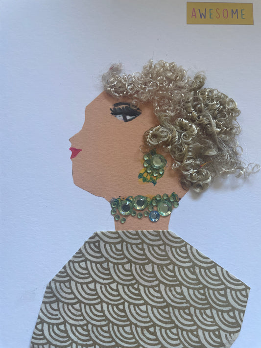 I handmade this card of a woman named Awesome Lemonade. She’s shown in profile with shimmering silver curls, dramatic lashes, and soft red lips. Her earring and necklace are made of pale green rhinestones, adding an elegant sparkle. She wears a gold and cream geometric patterned garment. A small “AWESOME” sticker floats above her, perfectly matching her confident, graceful energy.