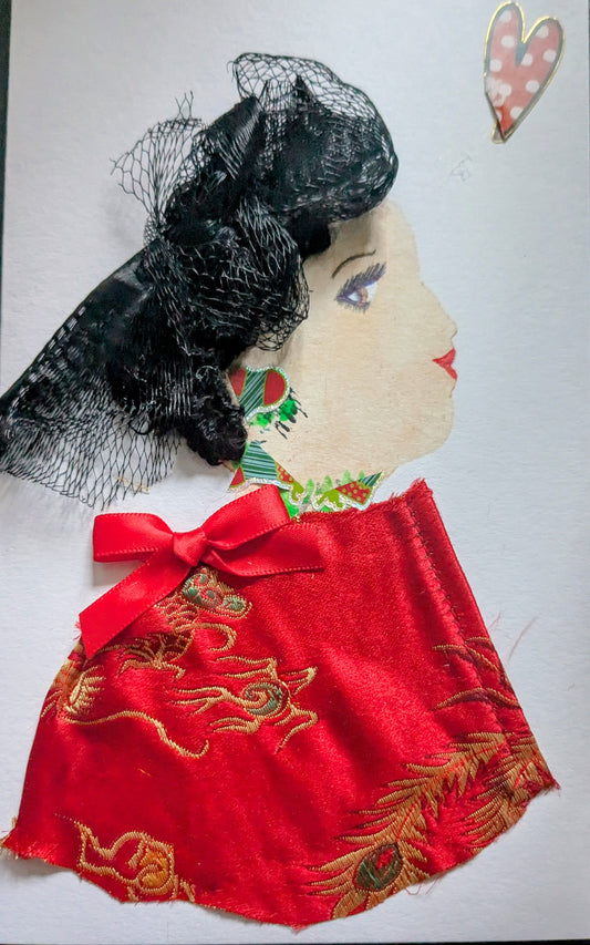 I handmade this card of a woman named Beaulieu Bellingham. She’s shown in profile with soft makeup, red lips, and delicate violet eyes. Her hair is styled in sculpted waves wrapped in black lace. She wears festive green and red paper jewellery around her ear and neck, and a luxurious red satin garment embroidered with golden dragons, finished with a neat red ribbon bow. A small heart sticker floats beside her.