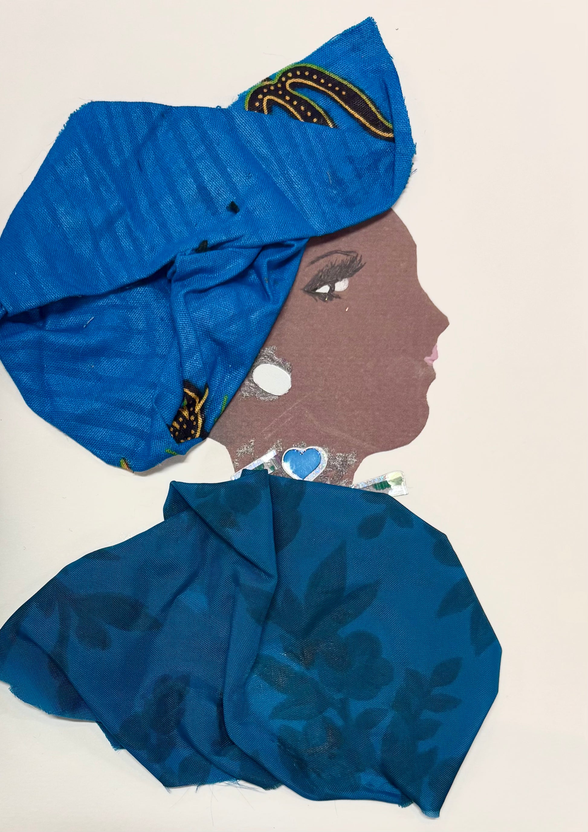 A woman wears a royal blue headwrap featuring a subtle stripe pattern. Her blouse is blue and features a monochromatic dark blue floral design. Her necklace has a blue heart and she wears a white earring.