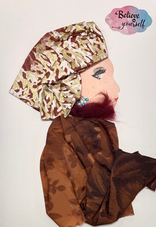 This is a handmade card of a woman named Brilliant Bree. She wears a red and gold patterned headwrap and a brown floral outfit. Her hair is dark red and curly. She has small blue and silver beads as earrings. The card has the words “Believe in yourself” at the top.