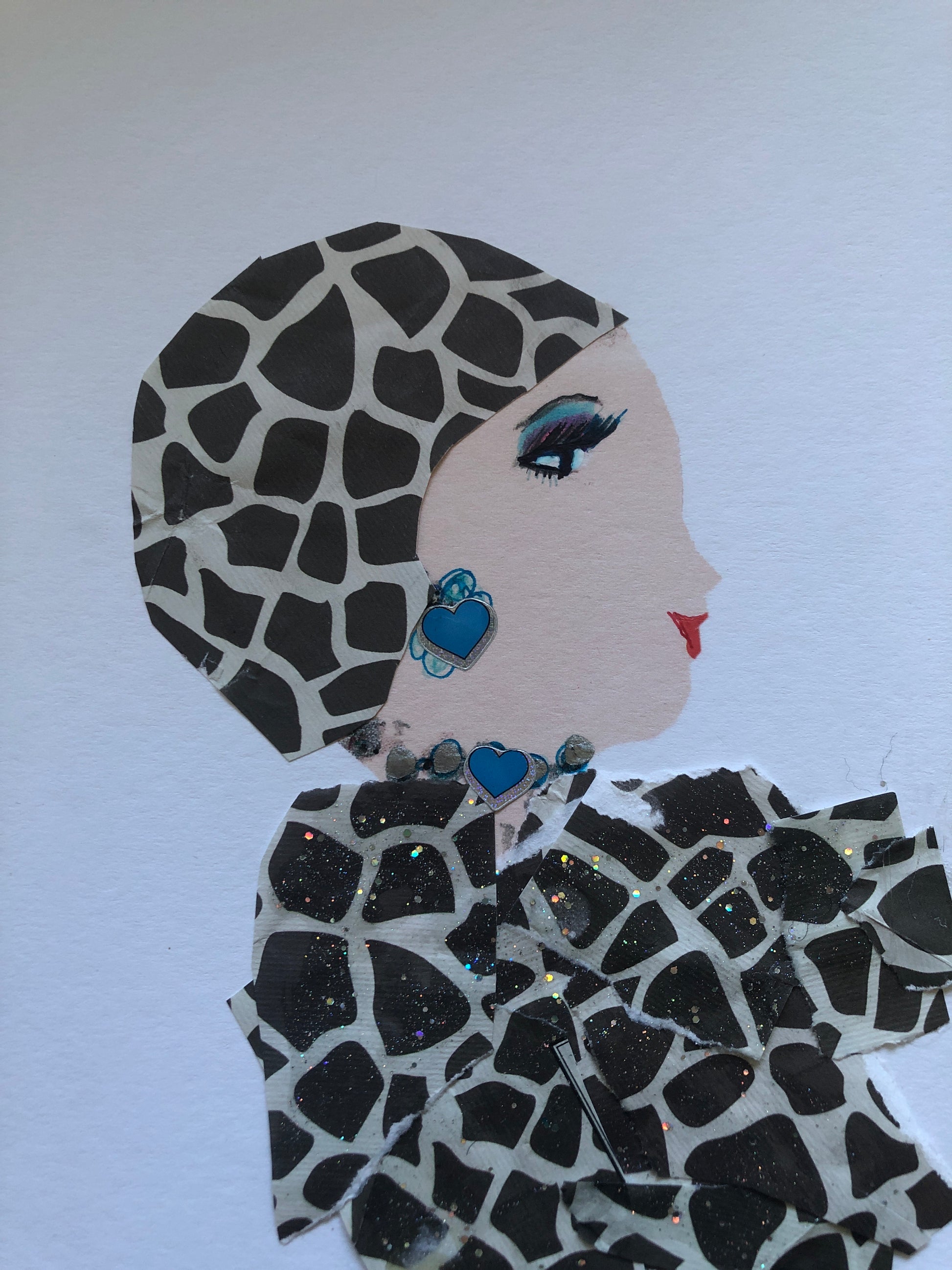 I handmade this card of a woman named Brilliant Peterlonia. She’s shown in profile with striking eye makeup, red lips, and a confident expression. Her outfit and headwrap are made from matching giraffe-print fabric with added sparkle. She wears a blue heart-shaped earring and a necklace with matching blue accents.