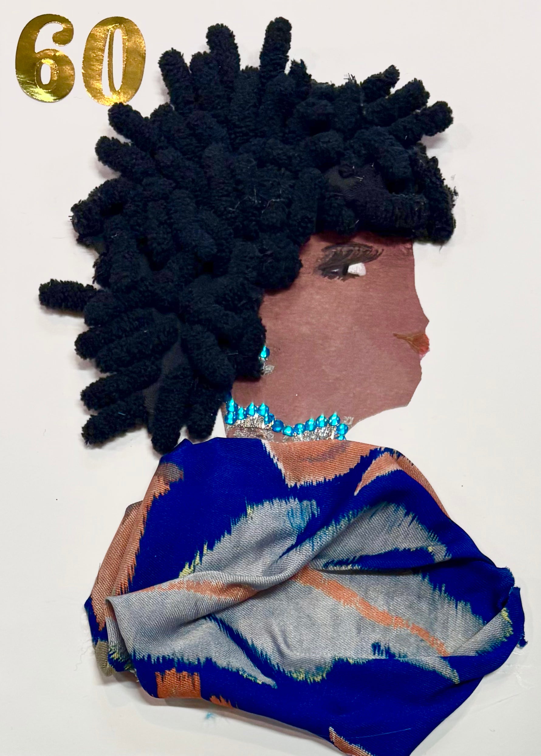 This is a handmade card of a woman named Brixton Bree. Her hair is made from thick black yarn styled in soft coils. She wears sparkling turquoise and silver jewellery. Her outfit is created from richly coloured fabric in blue, silver, and copper tones with a bold, flowing pattern. In the top corner, the number "60" is displayed in shiny gold lettering.