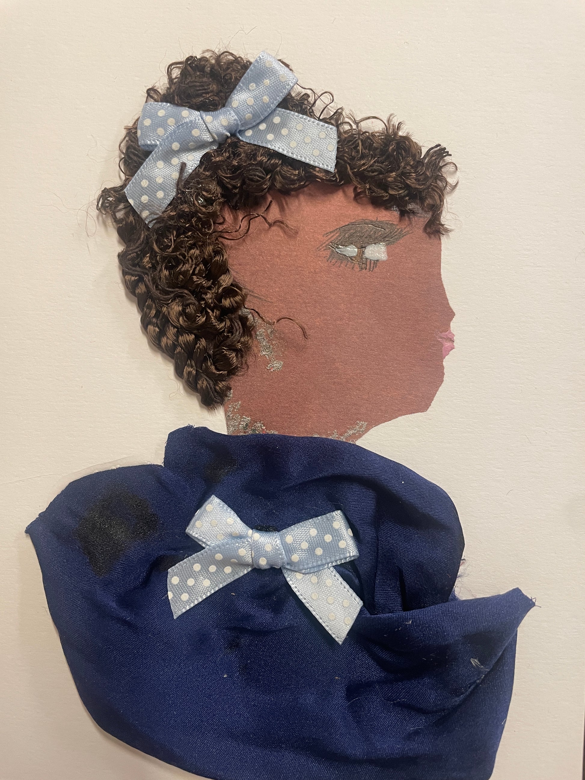 This is a handmade card of a woman named Charisse Clapham. She has tightly curled brown hair with a blue polka-dotted bow and wears a deep blue wrap with a matching bow on her shoulder.