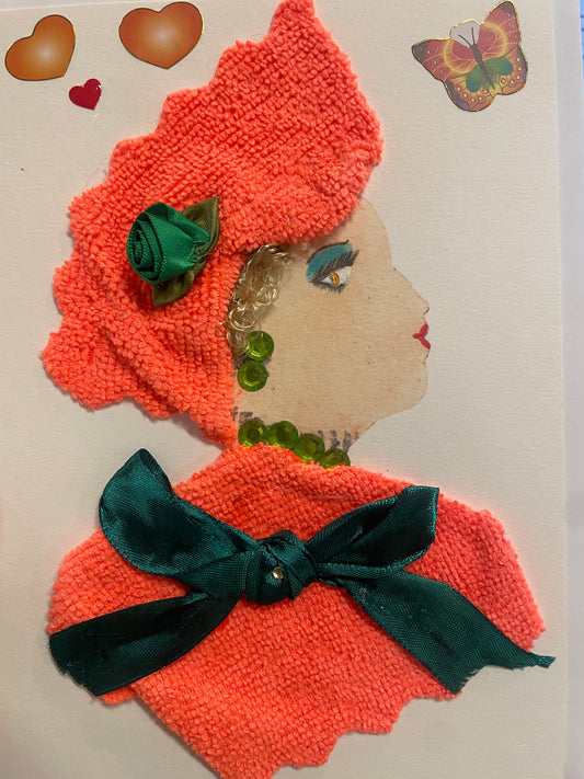 This is a handmade card of a woman named Chef Samantha. She wears a textured coral outfit with a matching hat and green satin bow, accessorised with green beads. Stickers of two hearts and a butterfly are in the background.