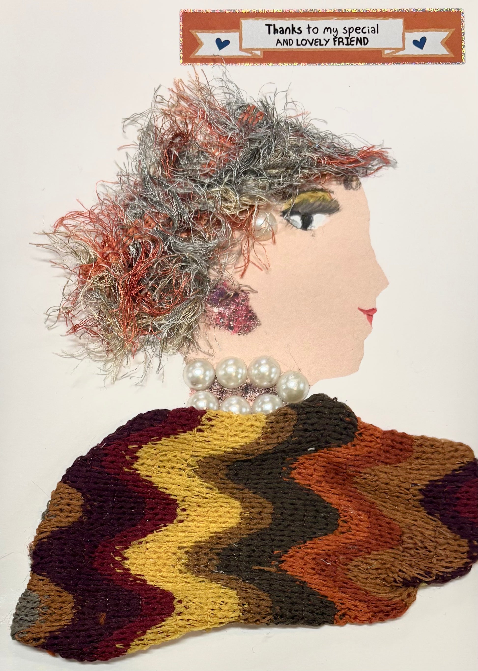 A woman wears a fuzzy hat with oranges and pale greens. Her blouse is made of a knit material with wavy lines featuring oranges, reds, and. yellow. She also wears a bright pearl jewellery. A sticker in the top right corner states "Thanks to my special and lovely friend."