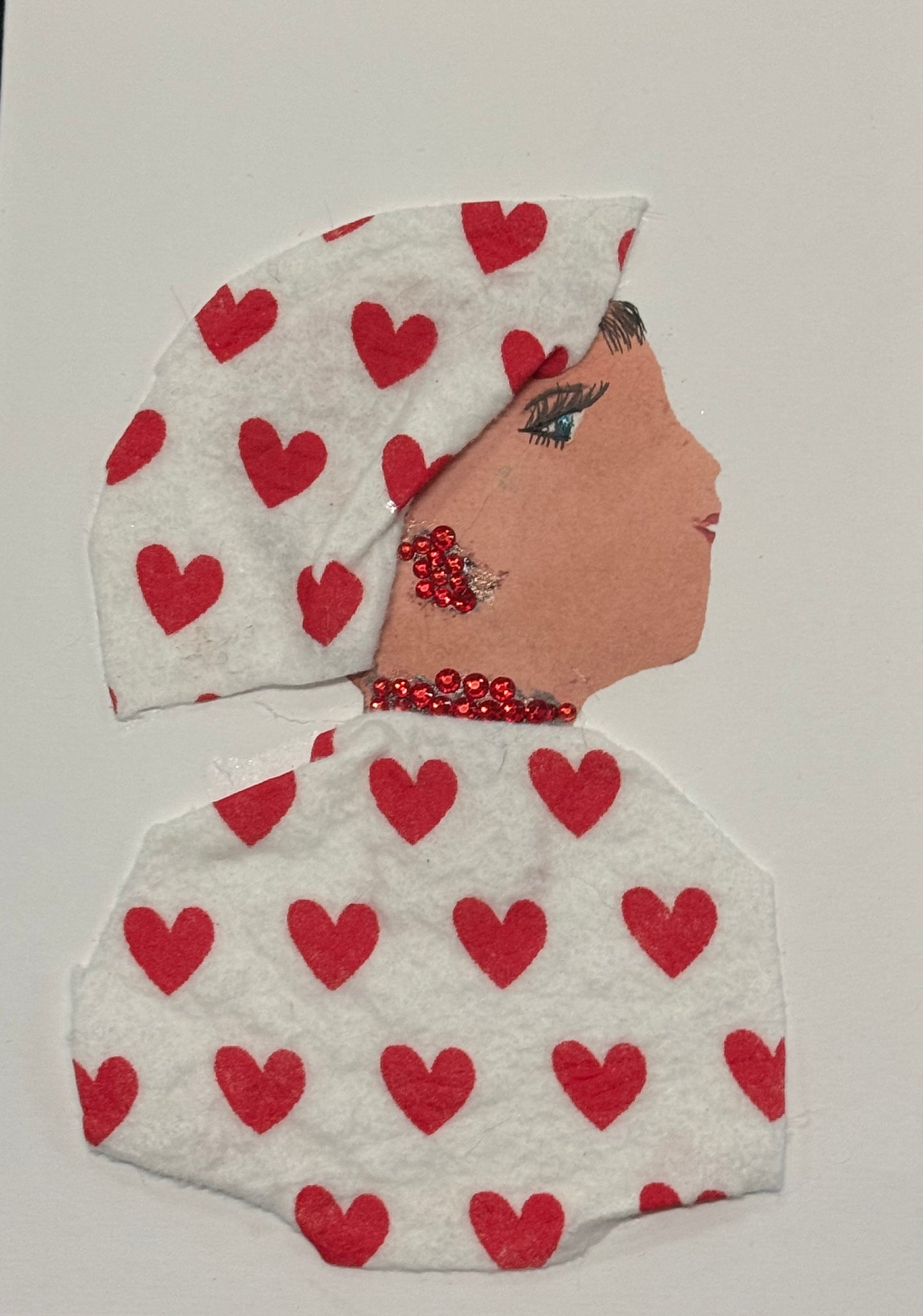 Handmade greeting card that doubles as a piece of art featuring a side-profile collage of a woman set against a clean white background. She wears a white headscarf and matching white outfit, both carefully decorated with evenly spaced small red heart patterns that create a soft, romantic rhythm across the design. Her jewelry includes bright red rhinestone earrings and a matching necklace that catch the light and add dimension to the otherwise minimal palette.