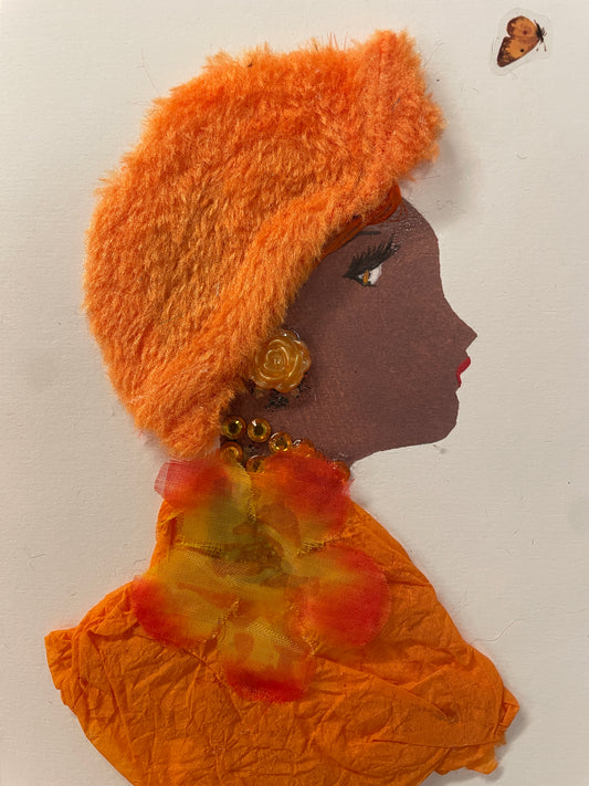 This is a handmade card of a woman named Delightful DiJonai. She wears a fluffy orange hat and wrap with a large golden-orange flower and matching beads.