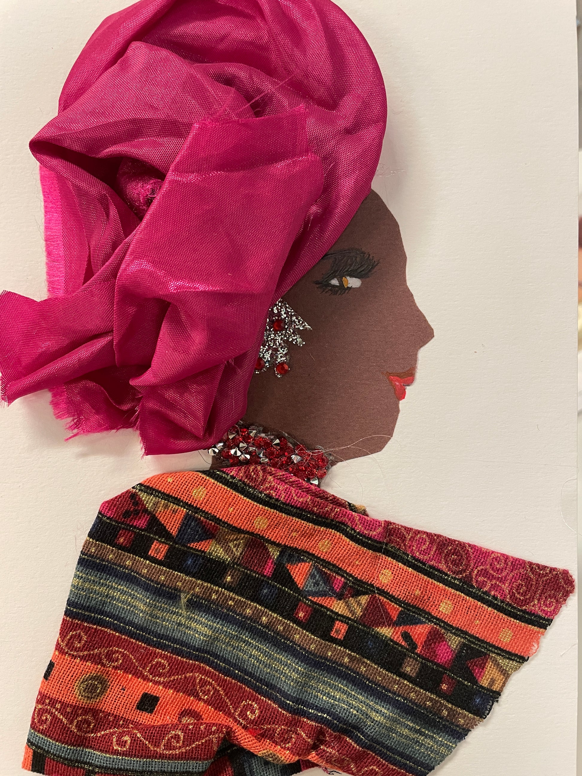 This is a handmade card of a woman named Dina Eastcourt. She wears a bright fuchsia wrap and glittering red jewellery, with a patterned red and black garment and bold makeup
