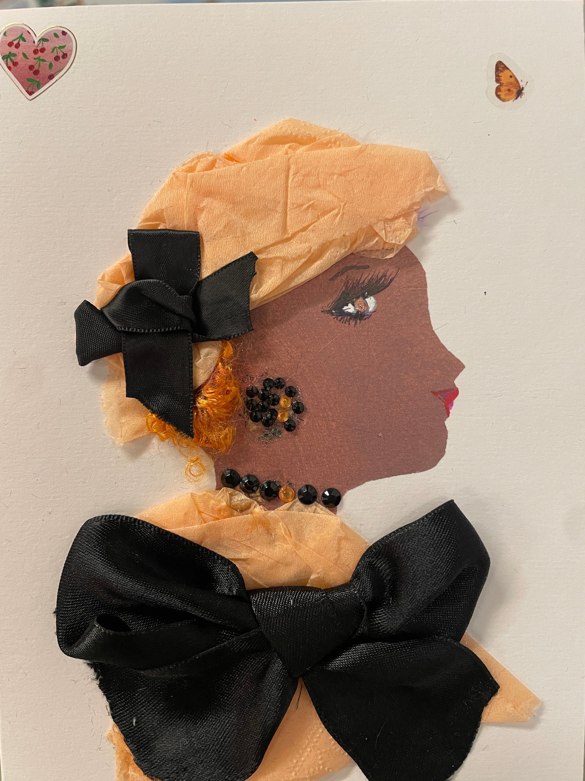 This is a handmade card of a woman named Dr. Jaelyn Junction. She wears a peach-coloured outfit and wrap with large black bows and sparkly black beads on her cheek and collar.