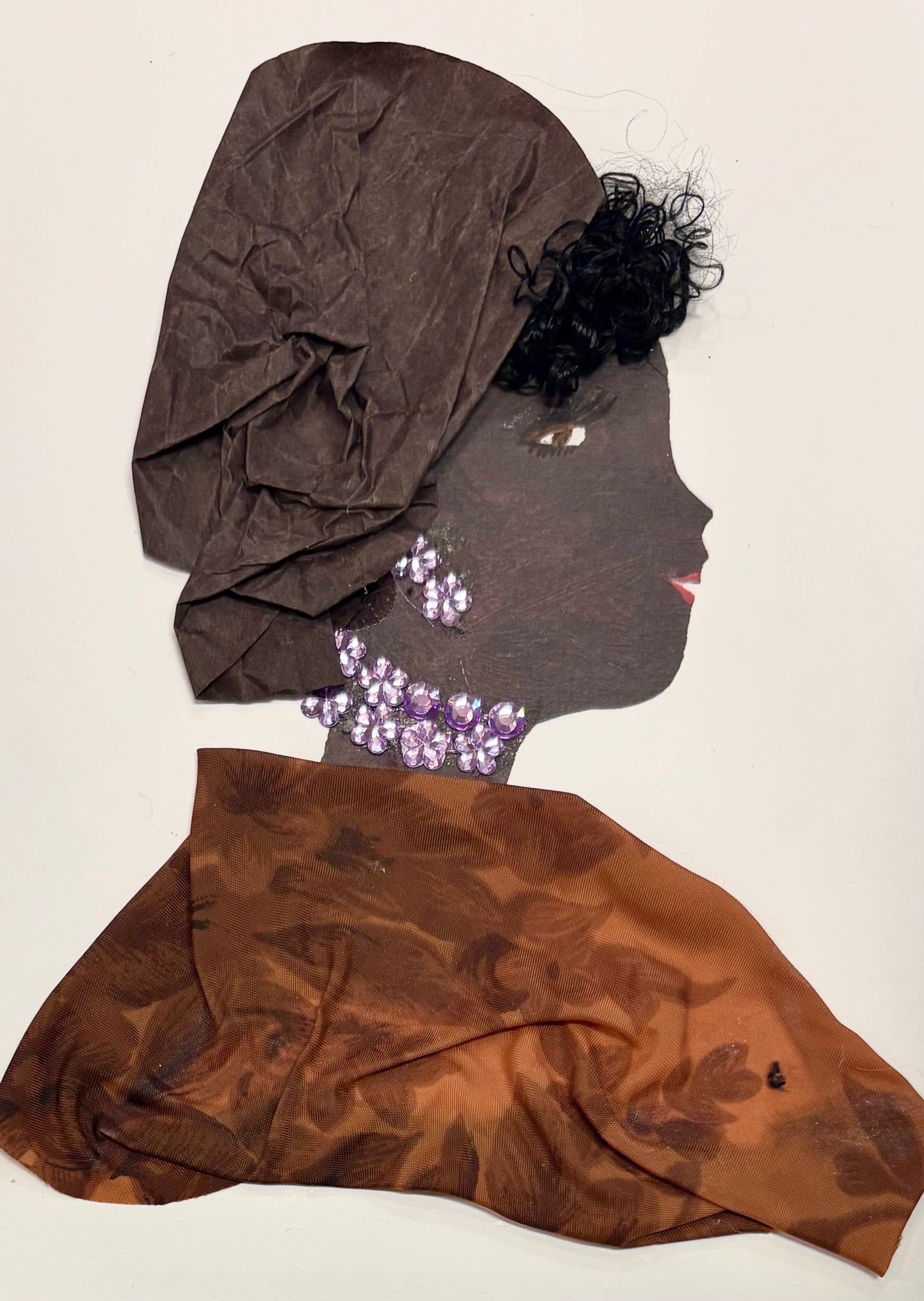 This is a handmade card of a woman named Dr Ella Elegant. She wears a tall brown headwrap made from soft, crinkled fabric and a flowing brown garment with a subtle floral pattern. Her jewelry is crafted from clustered purple gems arranged at her neck and ears. She has short, curly black hair peeking out and a serene expression with gentle eyes and red lips.