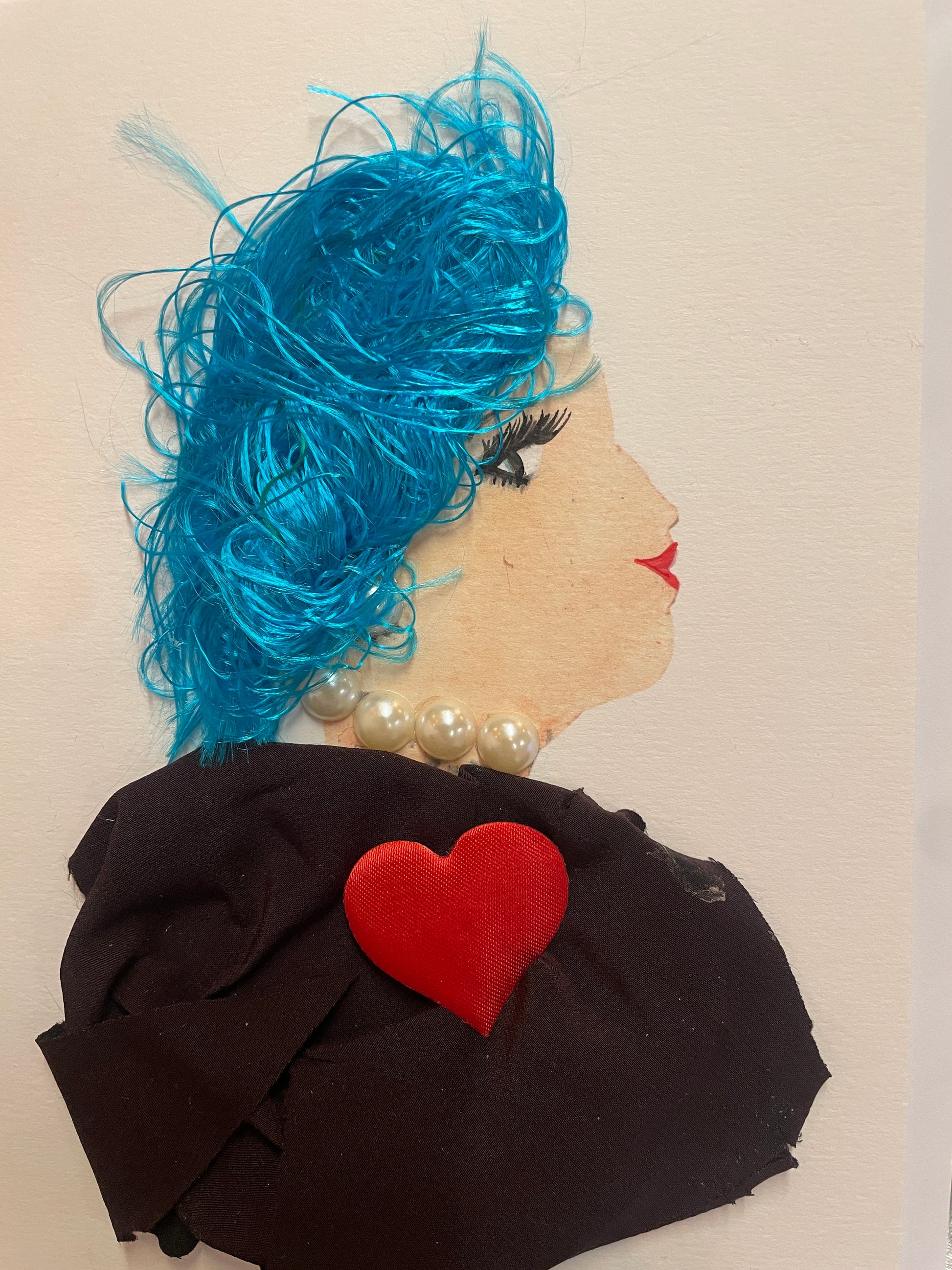 A handmade card of a woman in profile with electric blue textured hair, a pearl necklace, and a black garment with a red heart near the centre.