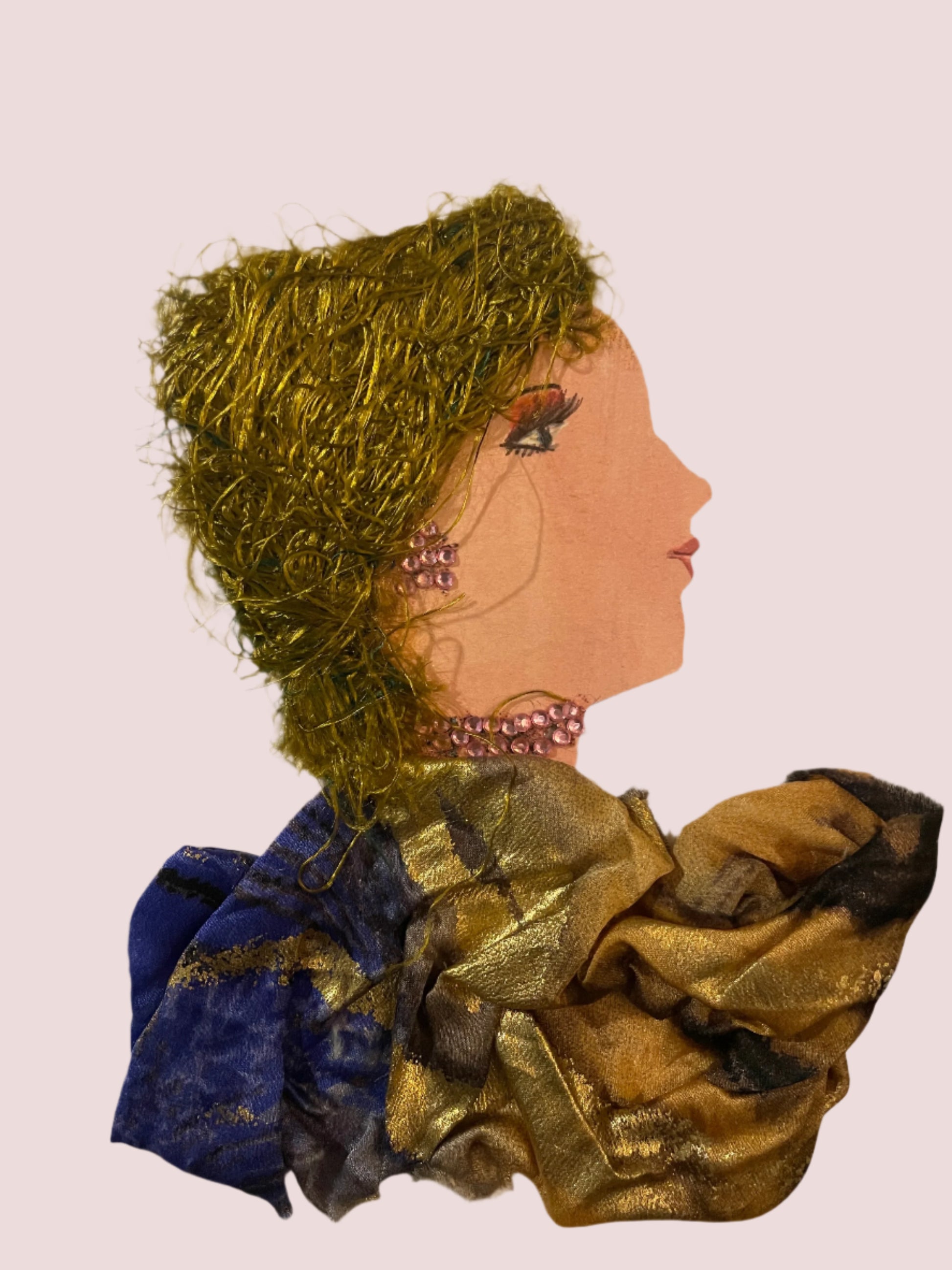 This is a handmade card of a woman named Ellie Goldborne. She has curly gold hair, wears a shiny gold and navy outfit, and has pink jewel details on her ear and neck.