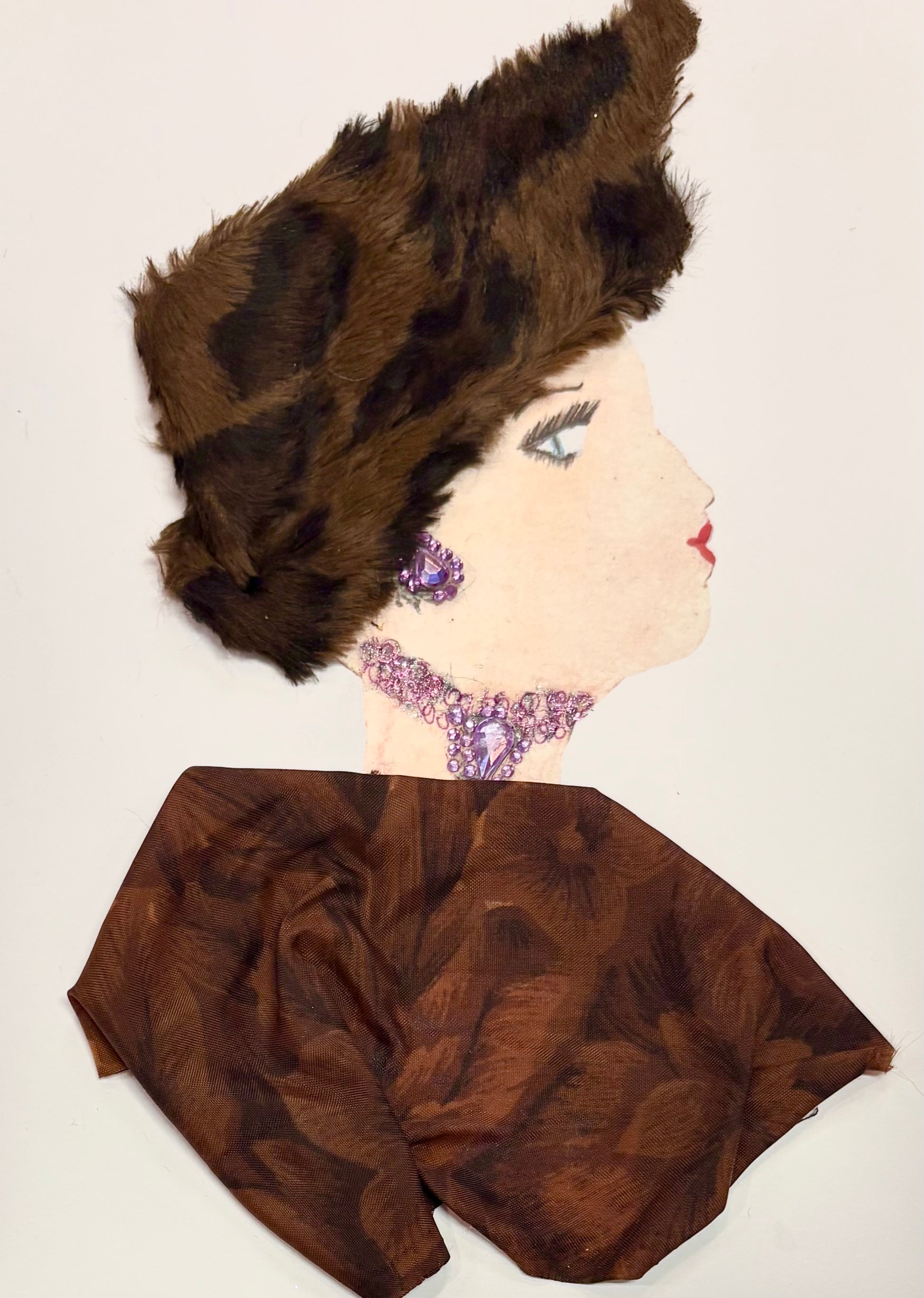 This is a handmade card of a woman named Embankment Ella. She wears a sculptural faux fur hat in rich brown with black accents, styled high and dramatic. Her earrings and necklace are made from purple gemstones, with the necklace forming a striking cluster at the base of her neck. Her outfit is a smooth, chocolate-brown fabric with a dark floral pattern, giving a classic and composed finish.