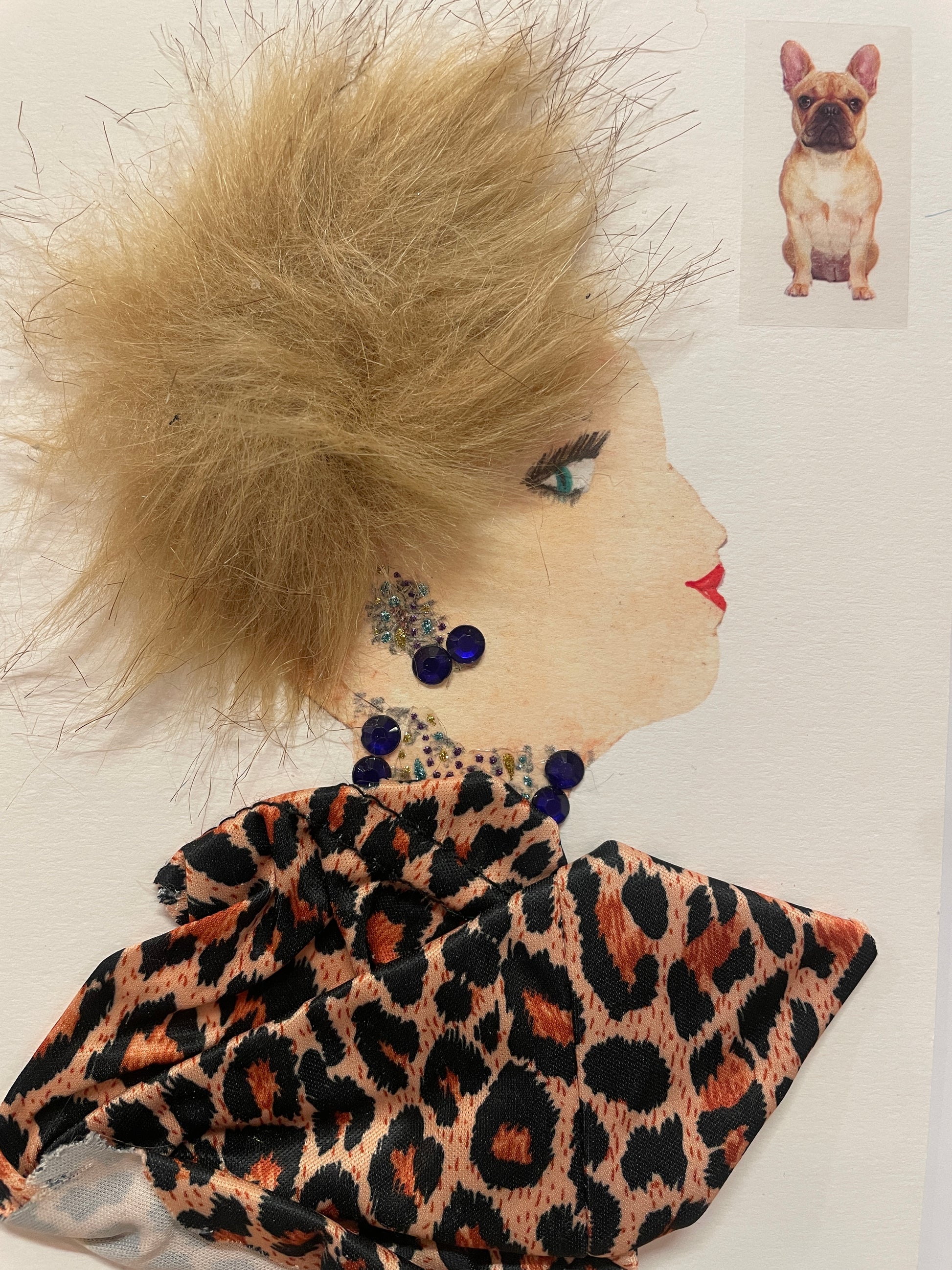 A handmade card of a woman named in profile with light brown faux-fur hair styled to stick outward. She wears dark blue gem earrings and a necklace, along with a copper-and-black leopard-print scarf. A French bulldog sticker is placed in the top right corner.