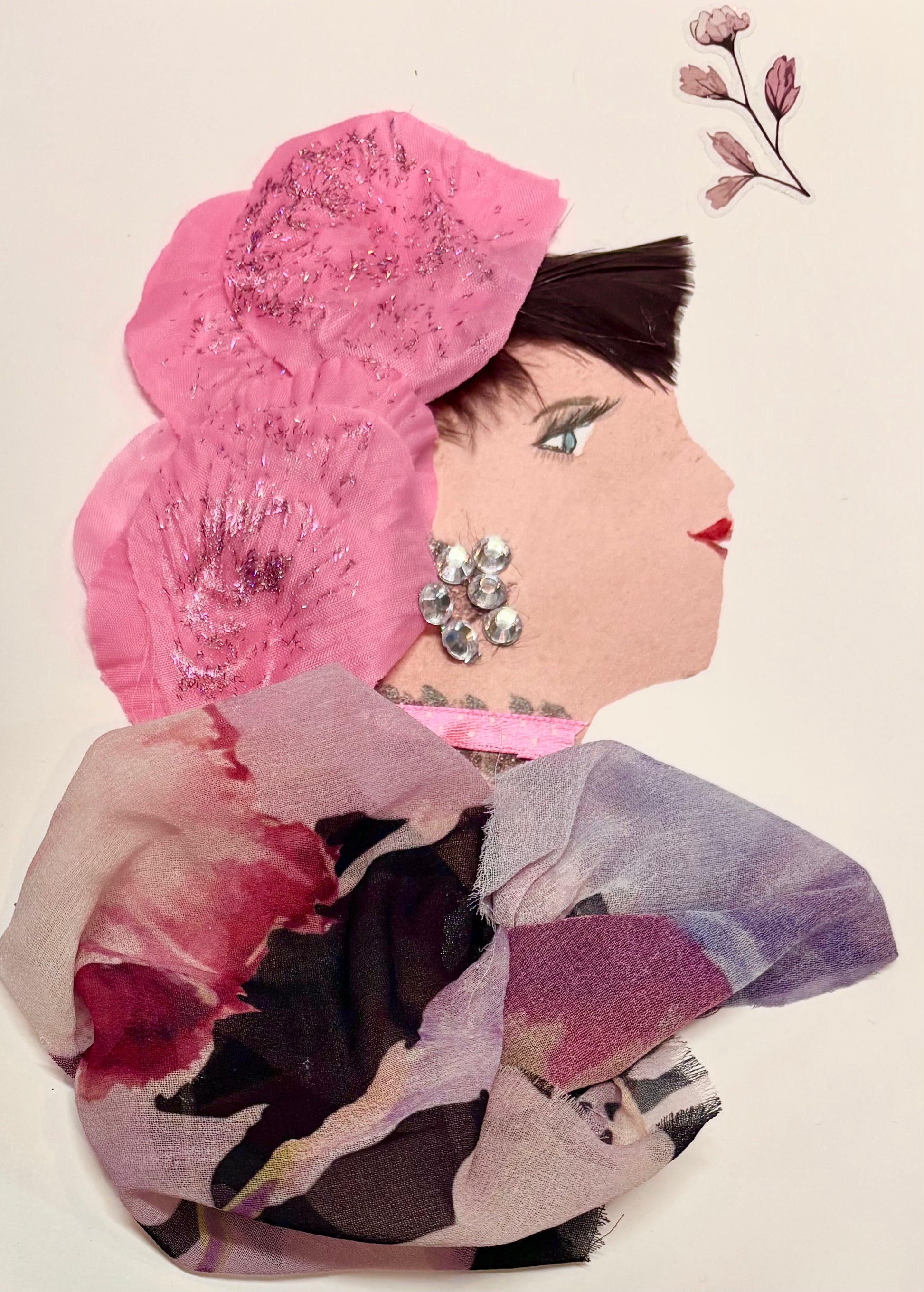 A woman wears a hat made of pink flower petals with a subtle sparkle. Her blouse has pinks, purples, and brown. She has silver gems as earrings and a pink ribbon necklace. There is a little pink flower in the top right corner of the card.