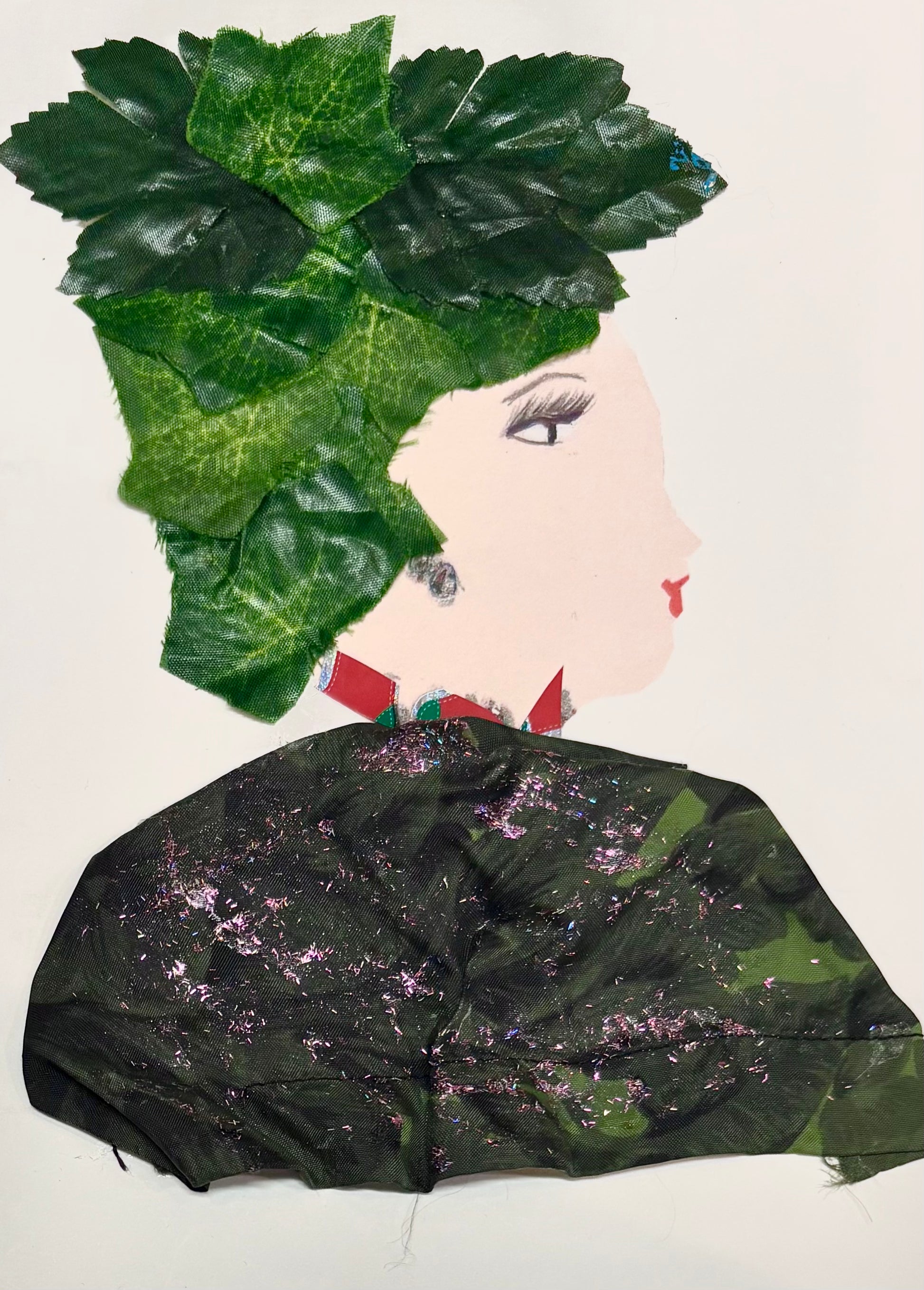 A woman wears green leaves as a hat and a dark green blouse with pink sparkles. She has a red necklace.