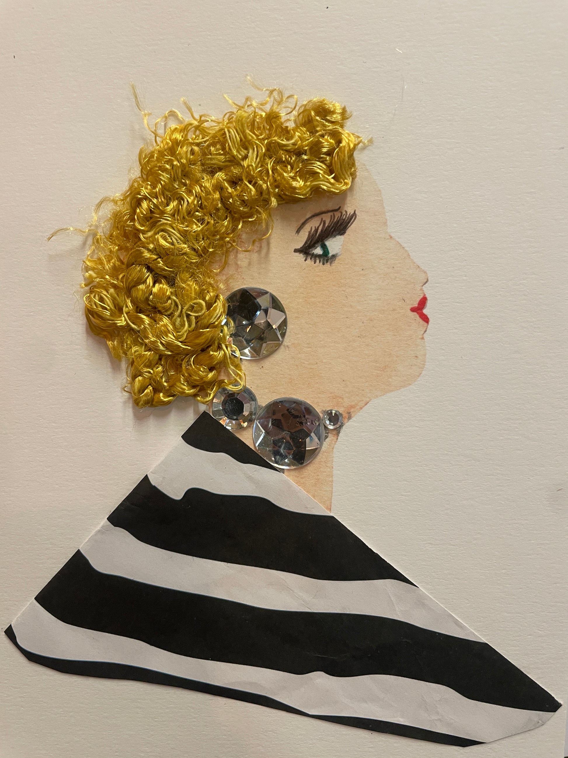 A handmade card of a woman in profile with curly golden hair and large silver gem earrings. She wears a bold black-and-white striped blouse.