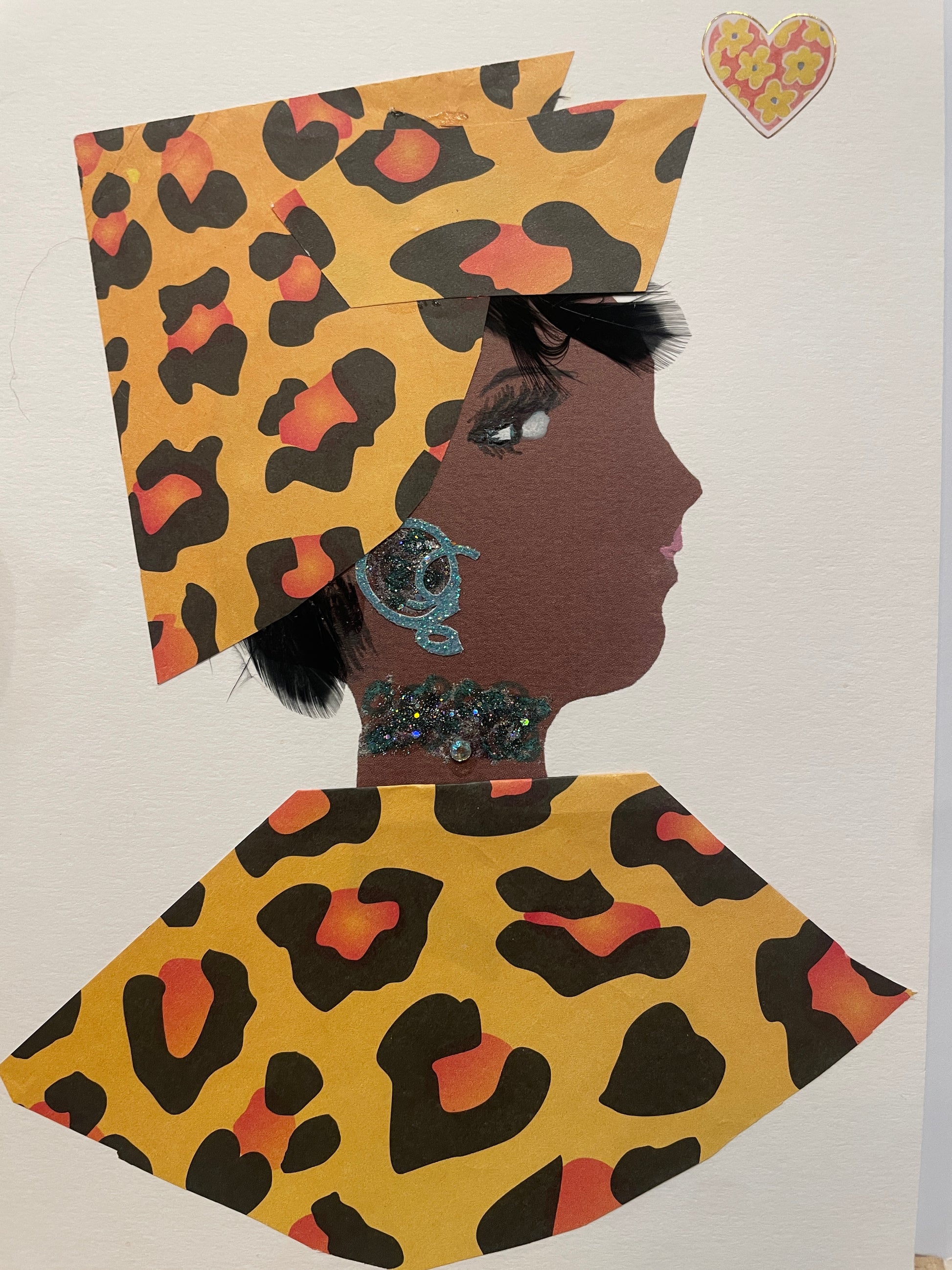 A handmade card showing a woman named Golden Giselle in profile dressed in golden-yellow and black leopard print clothing with a sharply folded headwrap. She wears a blue glittery earring and necklace, with a heart sticker nearby.