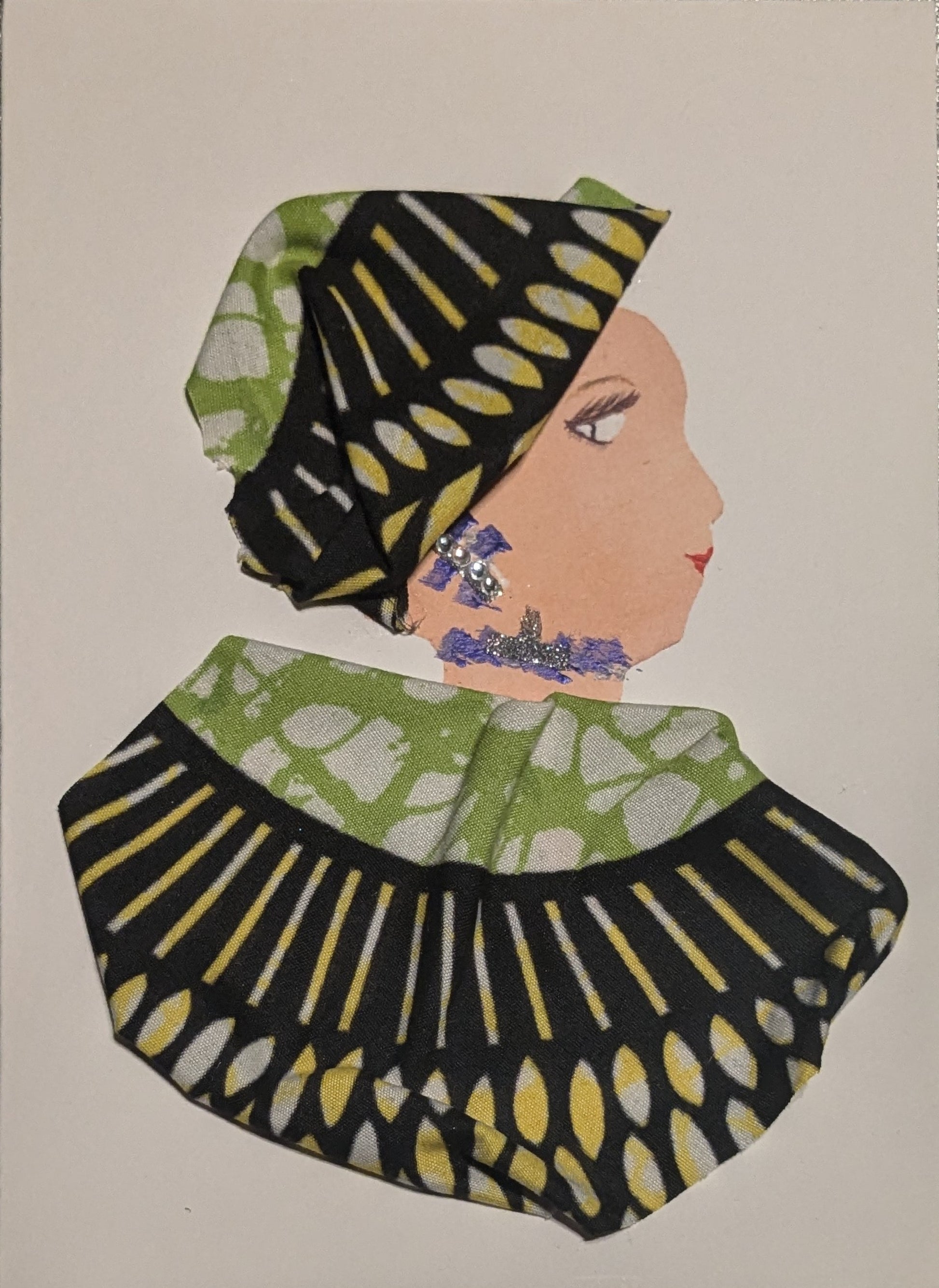 I handmade this card of a woman named Great Greenwoman. She’s shown in profile with a calm gaze, red lips, and a bold green, yellow, and black patterned headwrap and matching garment. Her jewellery features silver glitter and tiny pearl-like accents, with hand-drawn purple details on her ear and neckline.