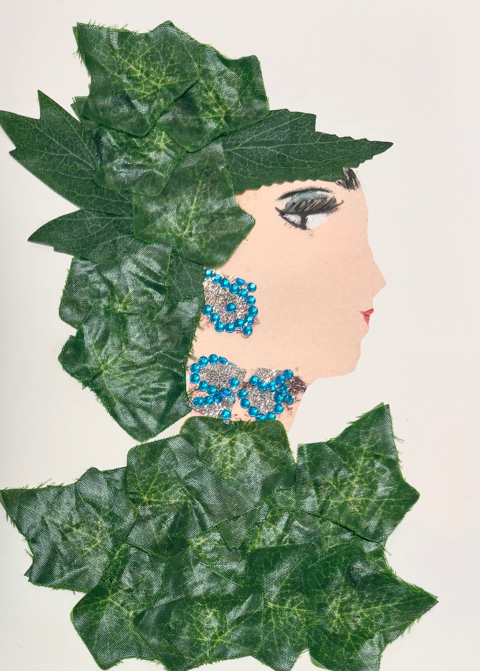 A woman wears leaves as a hat with a matching leaf blouse. Her jewellery is sparkling silver with little blue gems.
