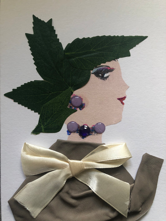 This is a handmade card of a woman named Hampstead Buffet. Her hair is made from green fabric leaves, shaped like a crown. She wears a soft grey-brown outfit tied with a cream-colored satin bow. Her jewelry includes round purple beads on her ear and around her neck.