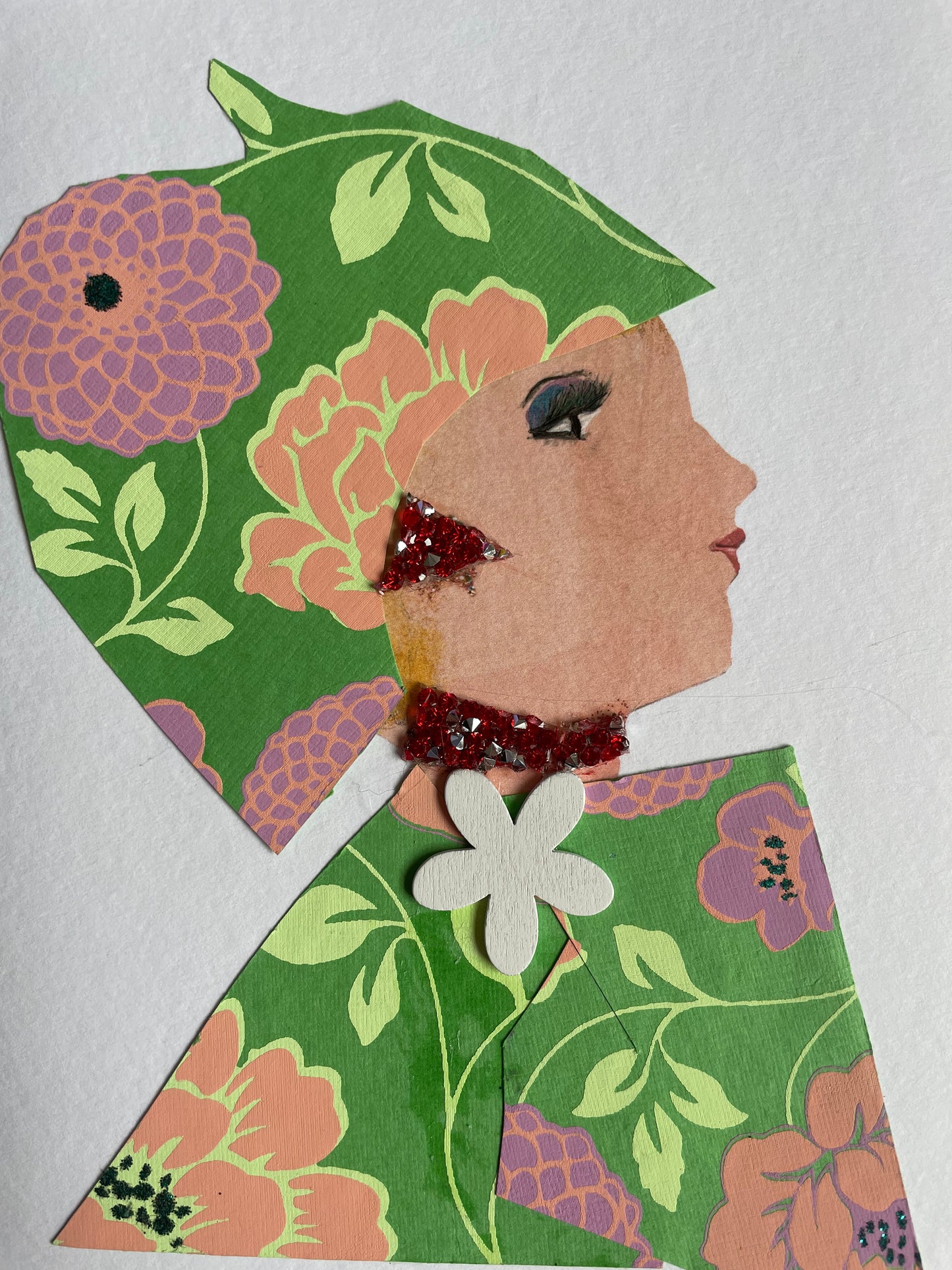 This is a handmade card of a woman named Hyde Park Poppy. She wears a matching hat and outfit made from green floral paper featuring bold pink, peach, and purple blooms. A red glitter earring and necklace add sparkle, and a white flower embellishment sits at the collar of her outfit.