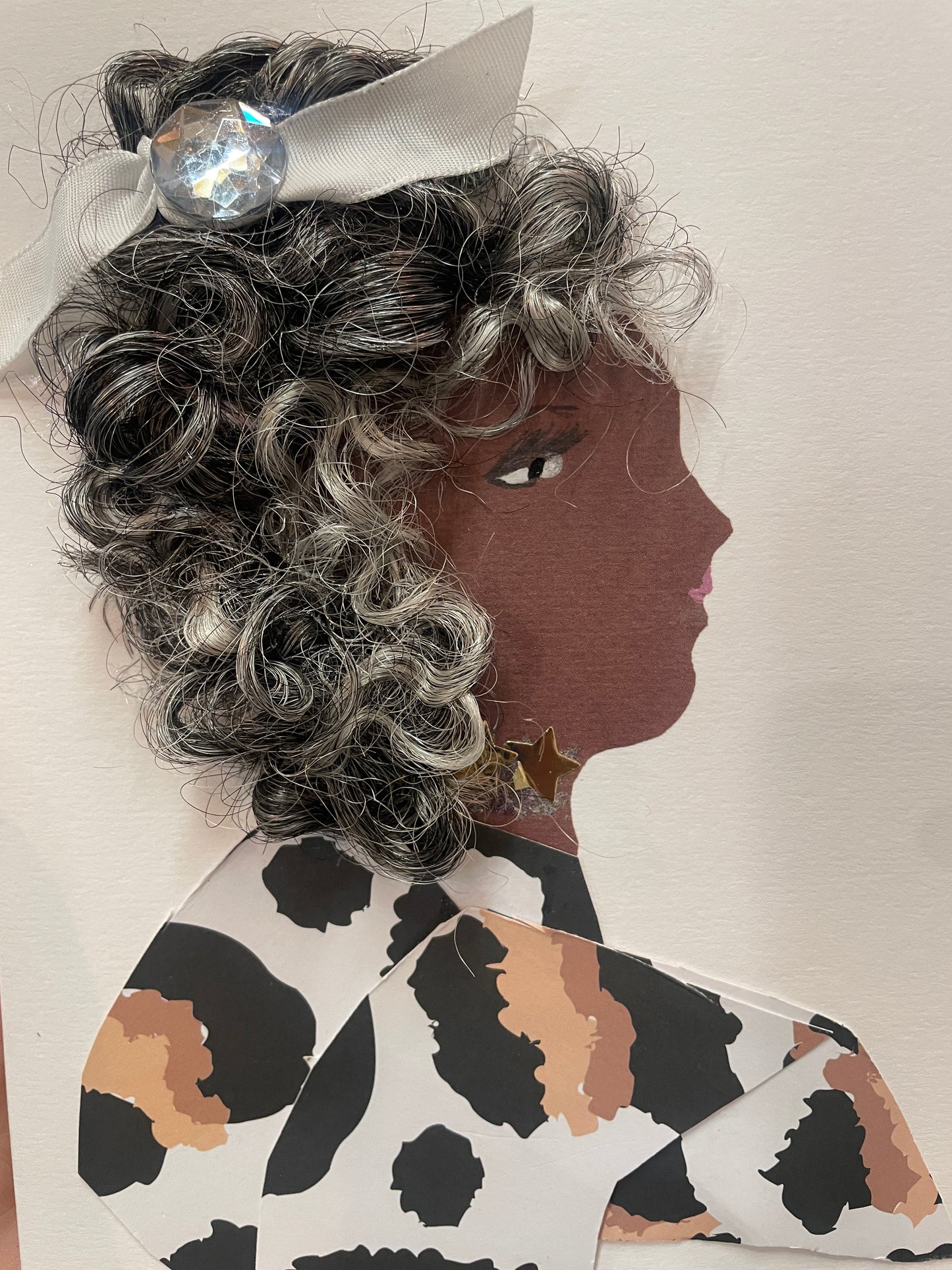 This is a handmade card of a woman named Rahi wearing a cow-print outfit. She has curly hair with silver highlights, a white ribbon with a gem, and gold star earrings.
