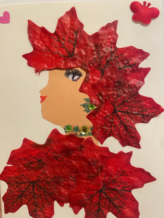 This is a handmade card of a woman named Maple Maida. Her hair and outfit are made from large red fabric leaves with black vein details, and she wears three green gem decorations at her neck. A red butterfly sticker and a pink heart are in the background.
