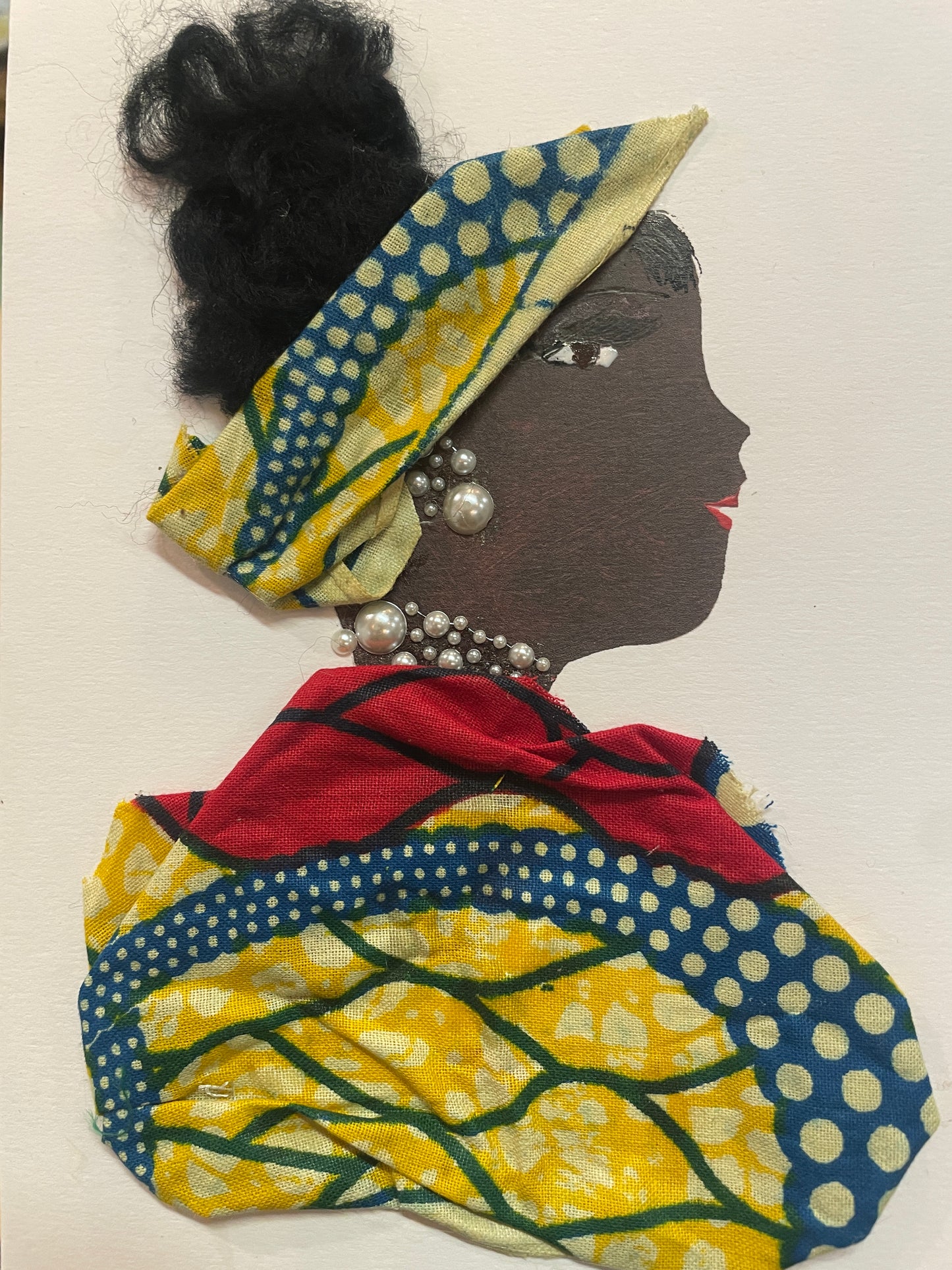 This is a handmade card of a woman named Kemi Kilburn. She wears a yellow Ankara-style headwrap and blouse, with black hair in a bun and pearl-like jewellery. The background is plain.
