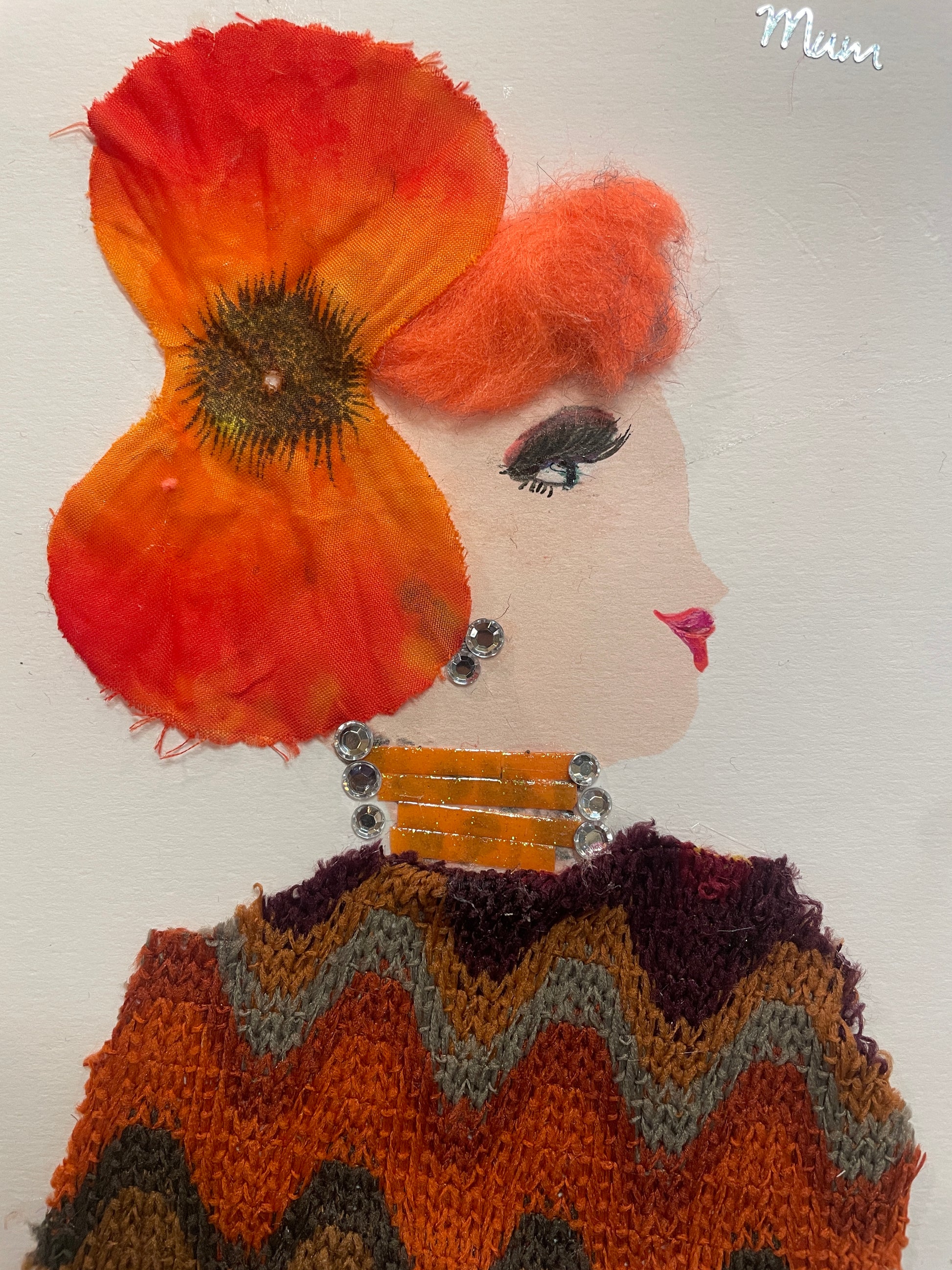 This is a handmade card of a woman named Marigold Mile End. She wears a fall-coloured knitted zig-zag blouse, a large orange hat, has orange hair, and the word “MUM” appears in the corner.