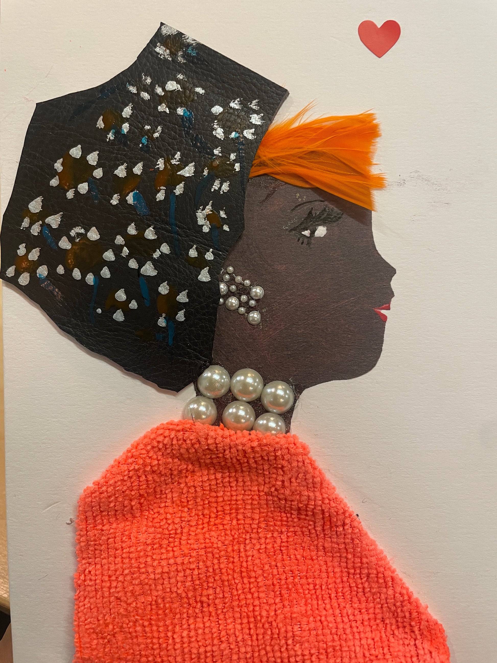 This is a handmade card of a woman named Solene Seaford. She wears an orange blouse, has orange hair, a black hat with painted flowers, and a red heart sticker in the corner.