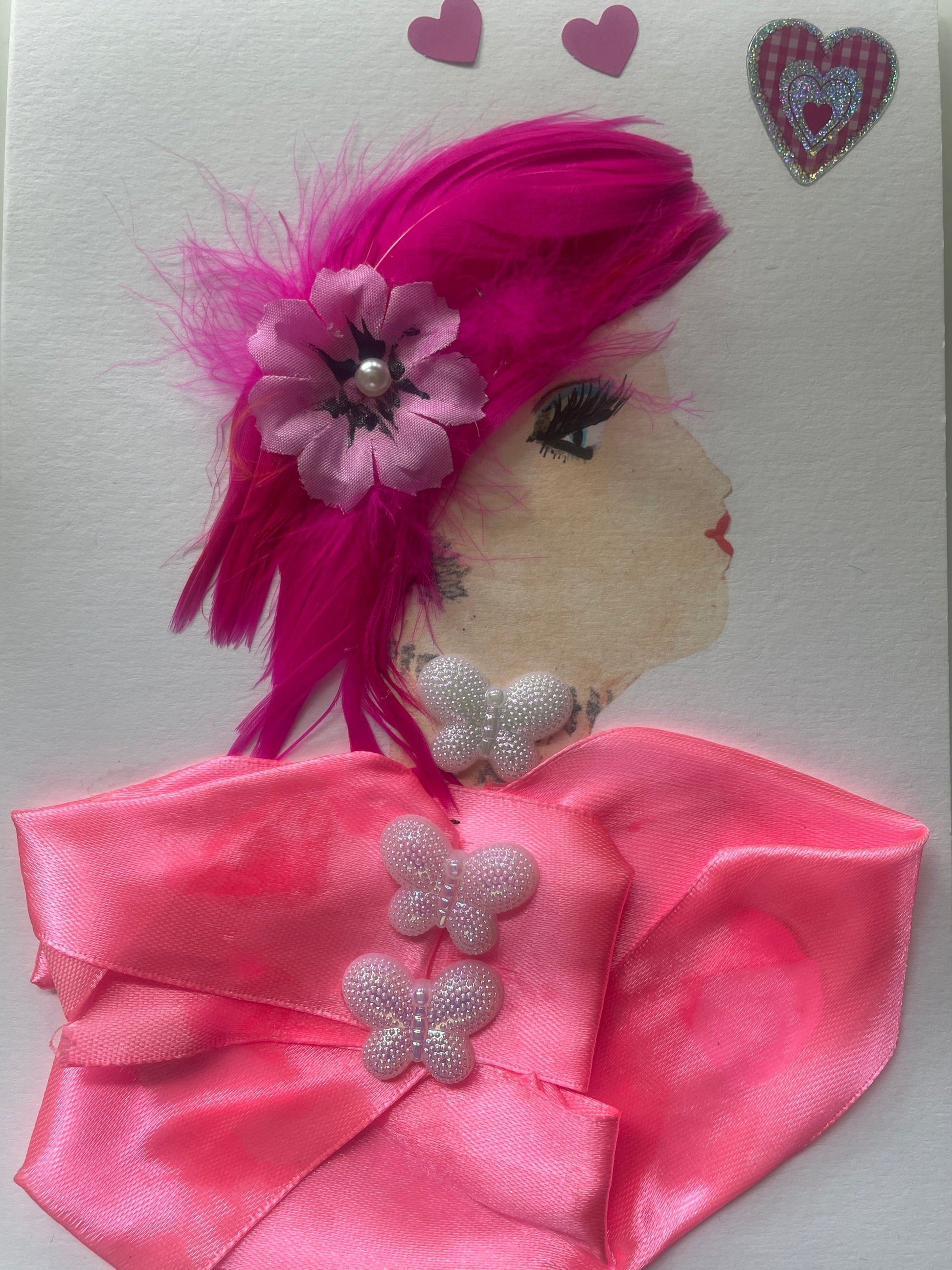 This is a handmade card of a woman named Fuchsia Finsbury. She has bright pink feathered hair with a flower, wears a pink ribboned blouse with three butterfly accents, and pink heart stickers in the background.