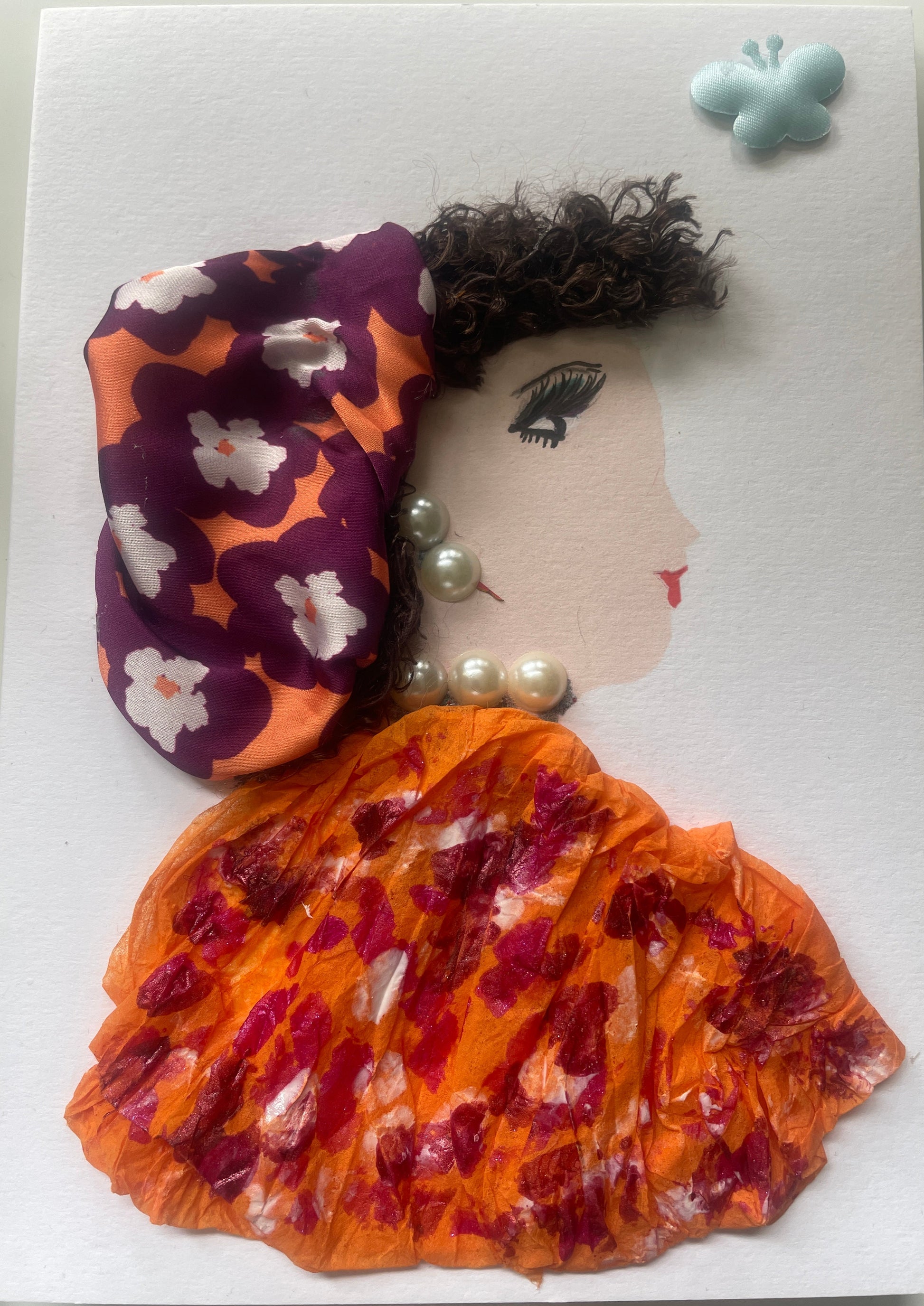 This is a handmade card of a woman named Paree Peckham. She wears a purple and orange floral headwrap, an orange blouse with red prints, pearl jewellery, and a blue butterfly sticker in the corner.