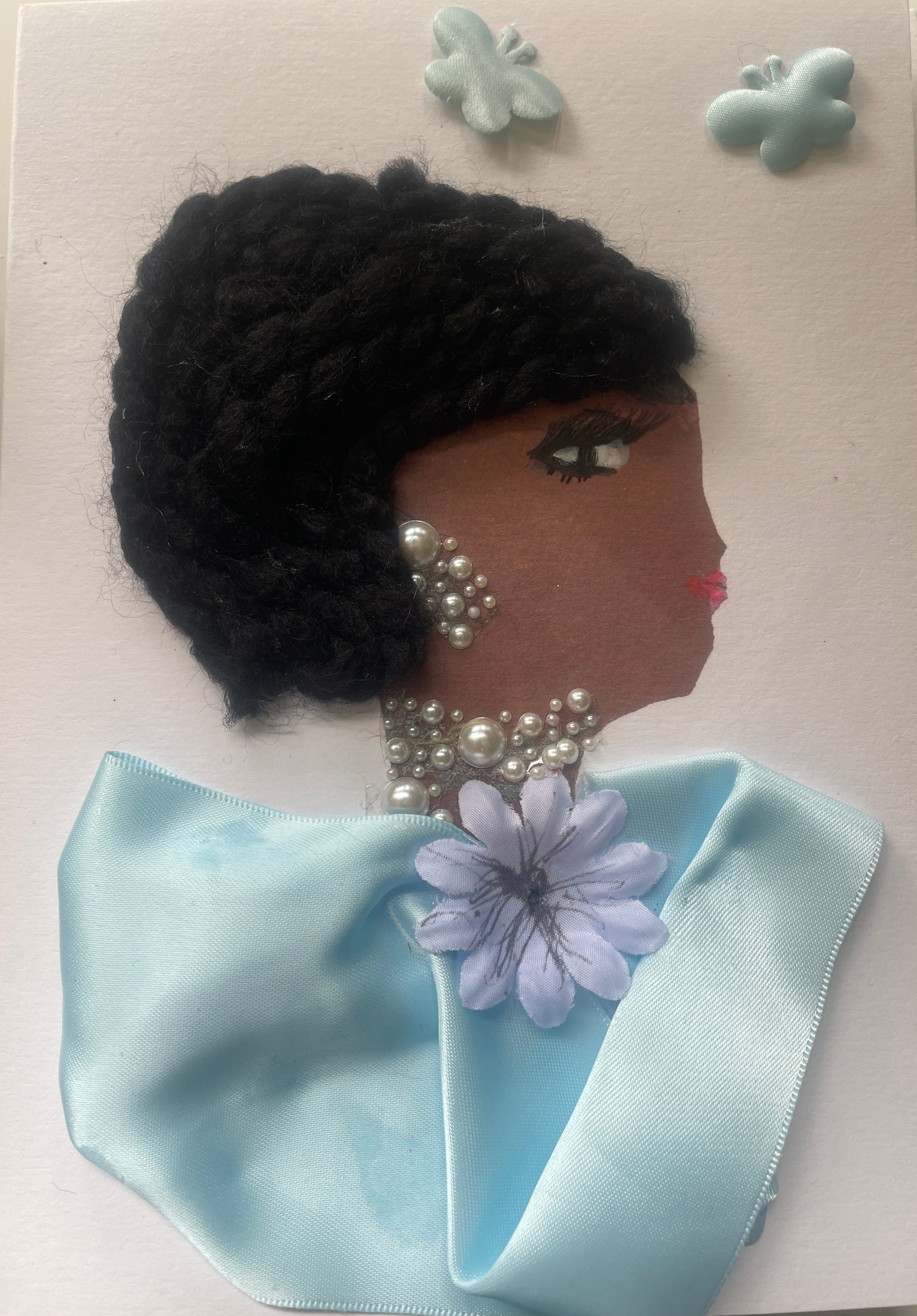 This is a handmade card of a woman named Skylar Sydenham. She has thick braided black hair, pearl jewellery, a light blue satin wrap with a lavender flower, and three butterfly stickers in the corner.