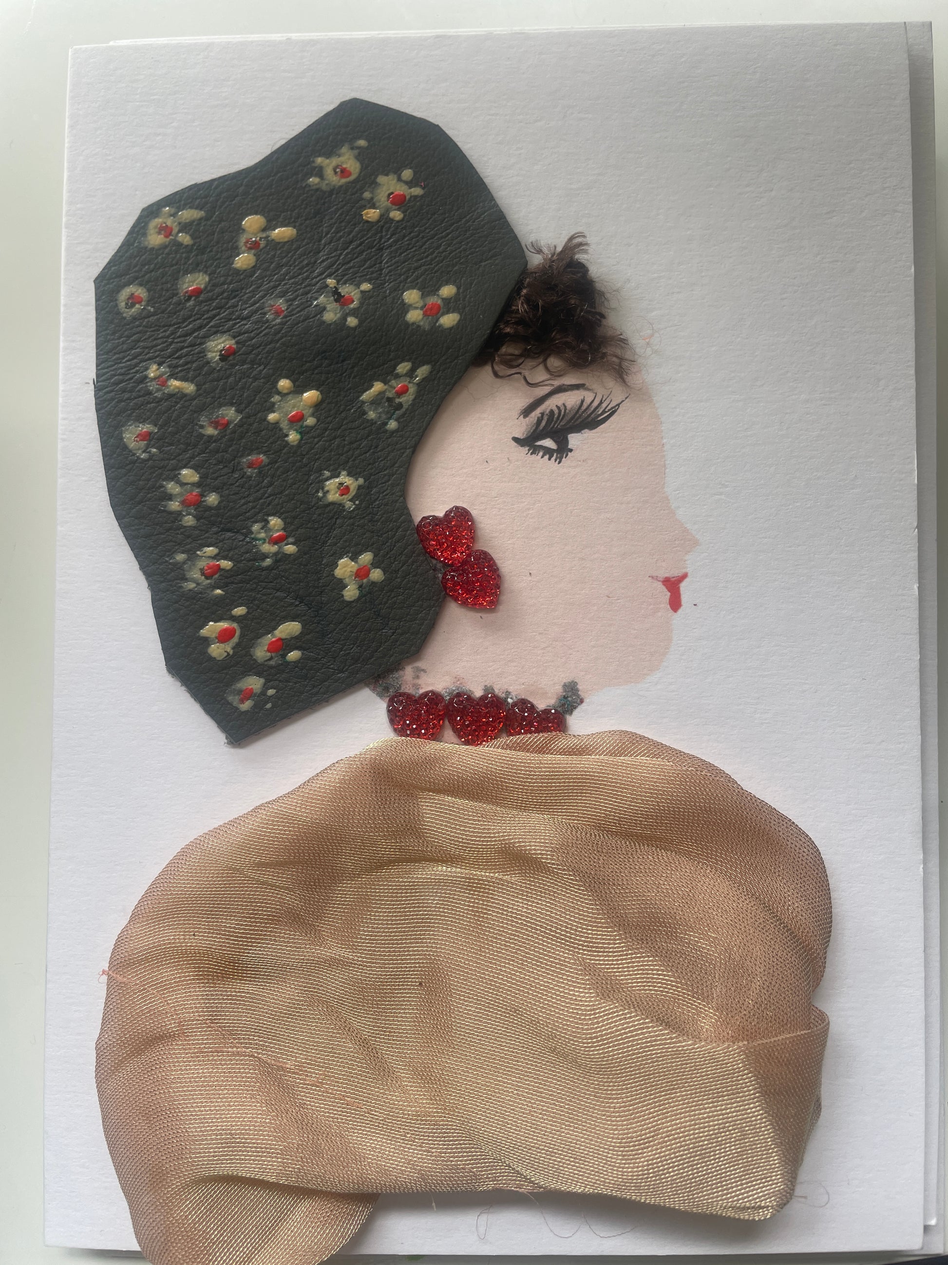 This is a handmade card of a woman named Honey Holloway. She wears a light beige wrap, a dark green headwrap with painted flowers, red heart earrings, and a soft red necklace.