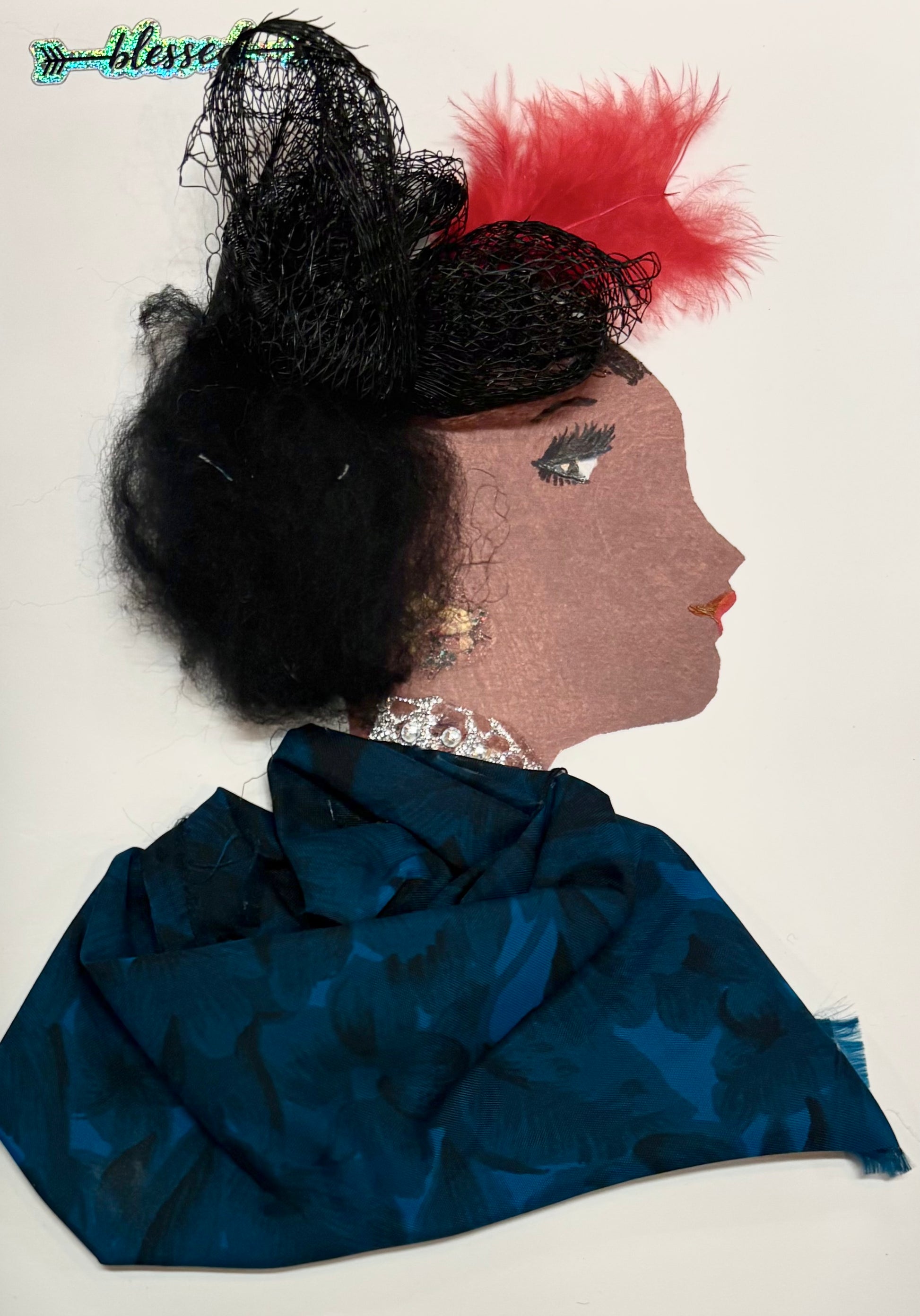 A side profile of a woman's face created with mixed media. She has curly black hair decorated with a black mesh hat and a red feather. She wears a sparkly earring and necklace, and her outfit is made from deep blue patterned fabric. Her eye and lips are drawn on, and the word "blessed" appears at the top left.