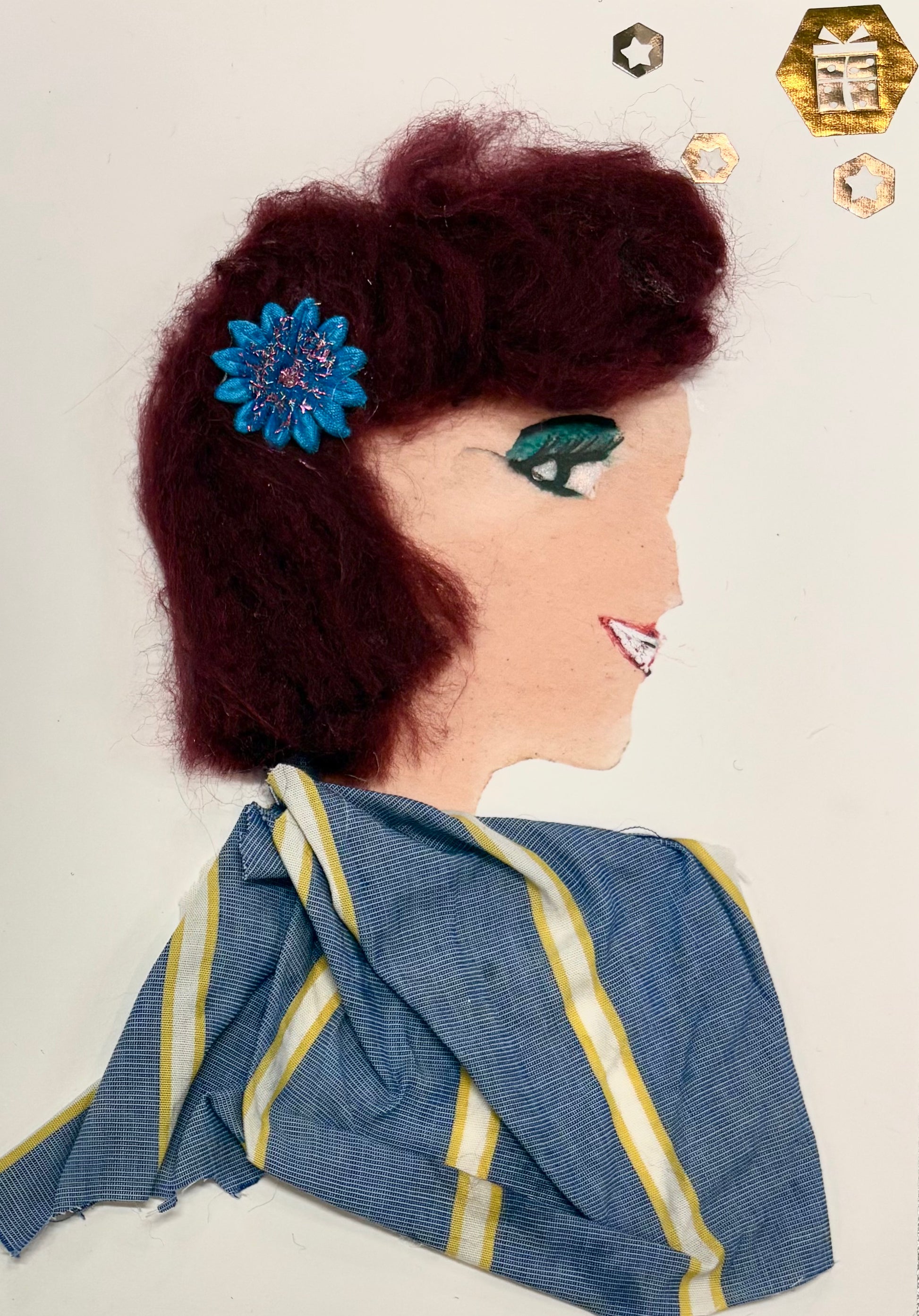 A side profile of a woman made with art materials. She has textured maroon hair with a shiny blue flower accessory. Her eye has bold green makeup, and her smile is drawn in white and red. She wears a blue fabric top with yellow and white stripes. Shiny gold and silver star-shaped decorations float near her head.