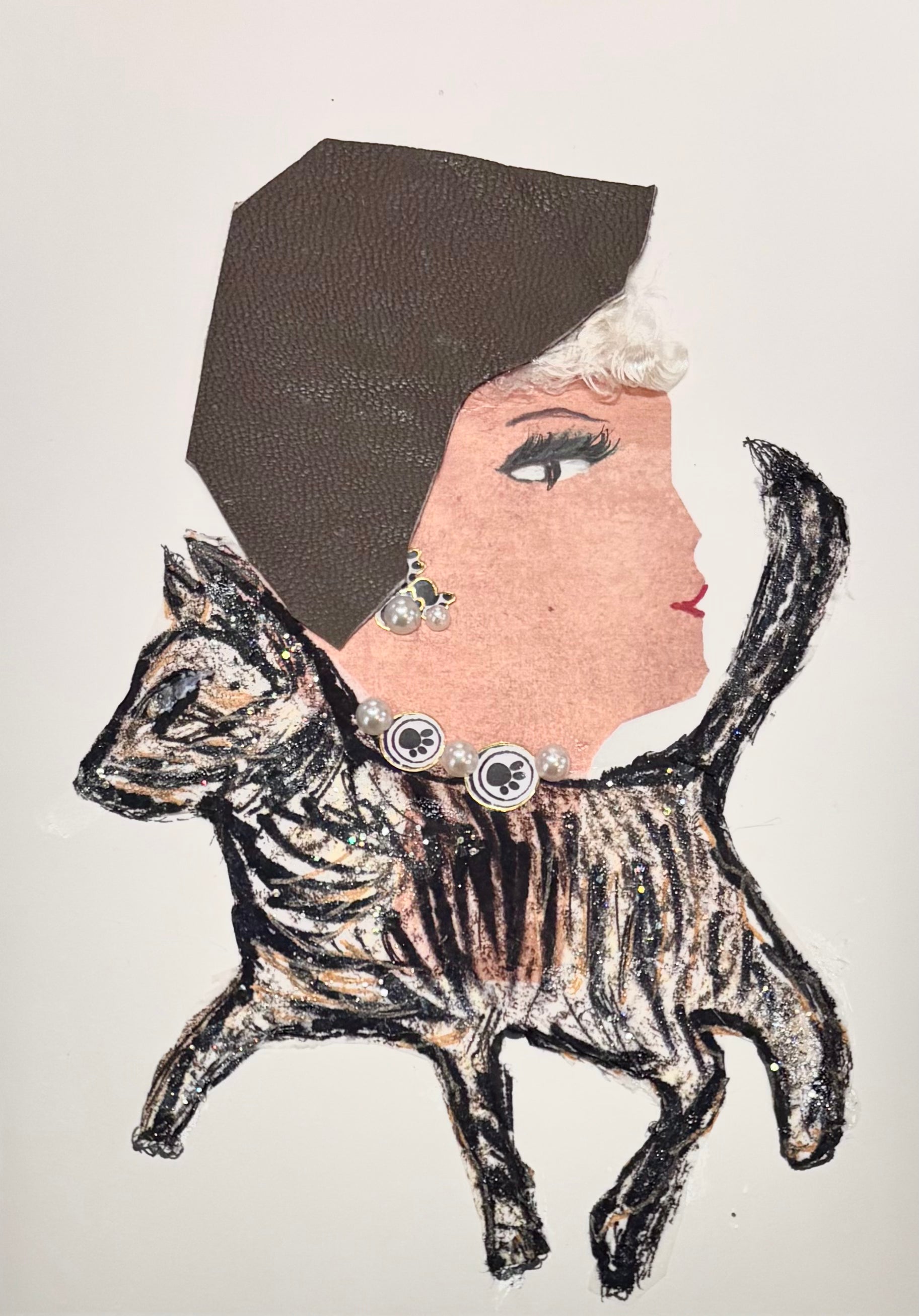 This is a handmade card of a woman named Kitty Katherine. Her outfit is creatively integrated with the illustration of a leaping tabby cat, whose body forms her dress. She wears a brown textured head wrap and has short, soft white curls peeking from underneath. Her necklace is made of pearls and round charms featuring black paw prints, echoing her feline theme. Matching earrings with a paw motif complete her playful, elegant look.