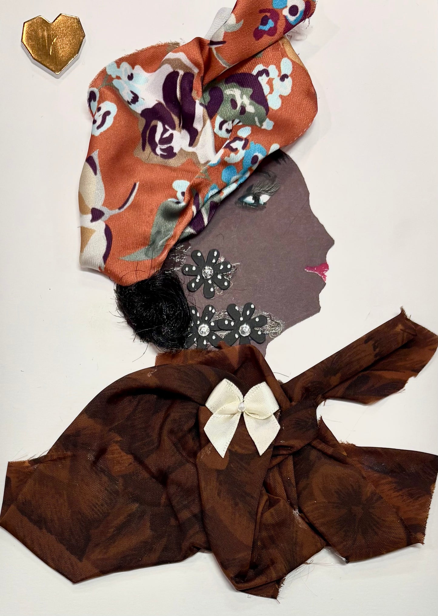 A woman wears an orange headwrap with a floral pattern. Her blouse is a chocolate brown feautirng a white bow in the center. Her earring and neckalce are made of black flowers. There is a gold heart in the top left corner of the card.