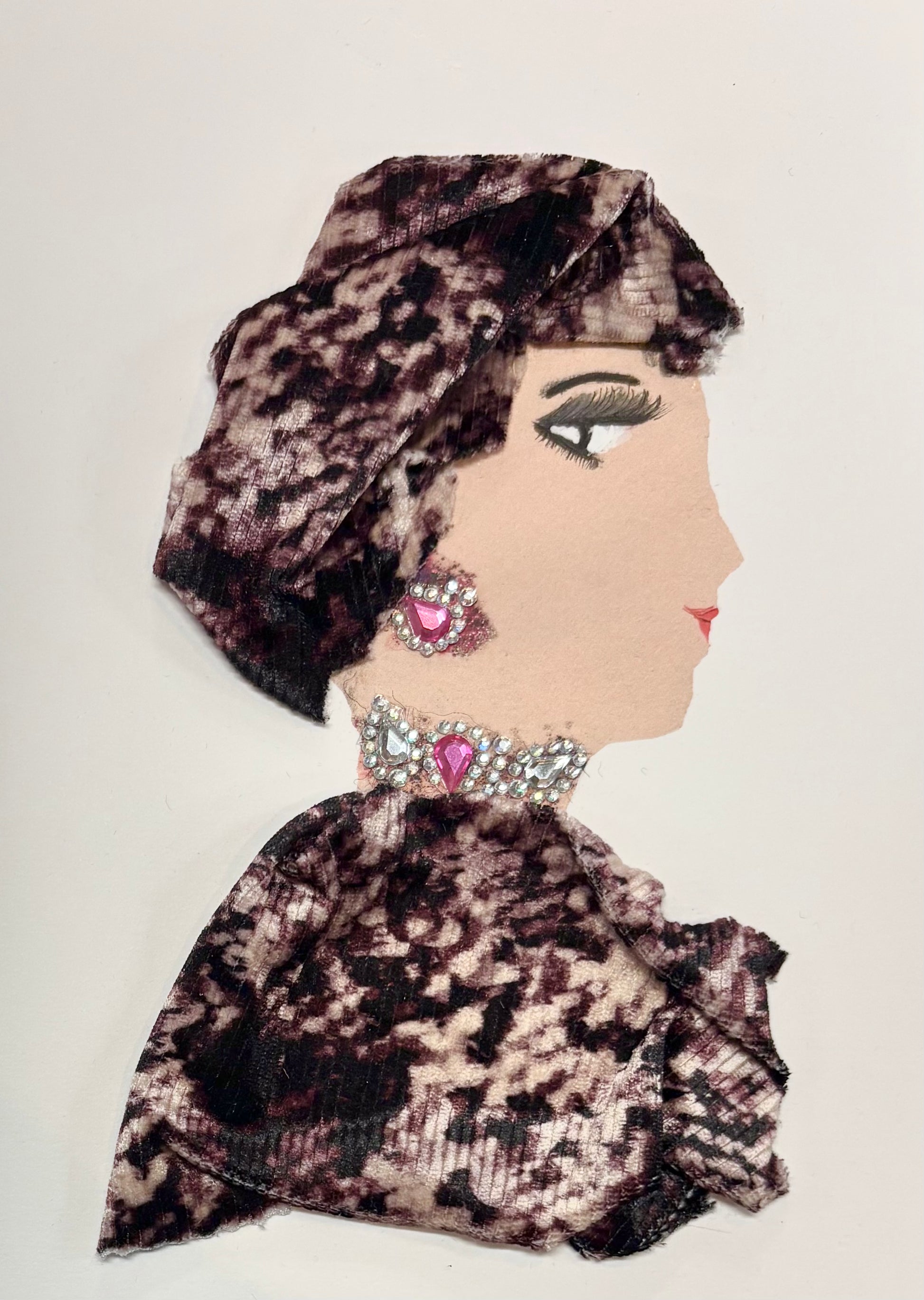 A woman wears a patterned headwrap and blouse with a mixure of creams and browns. Her jewellery is made up of little gems and two gems.