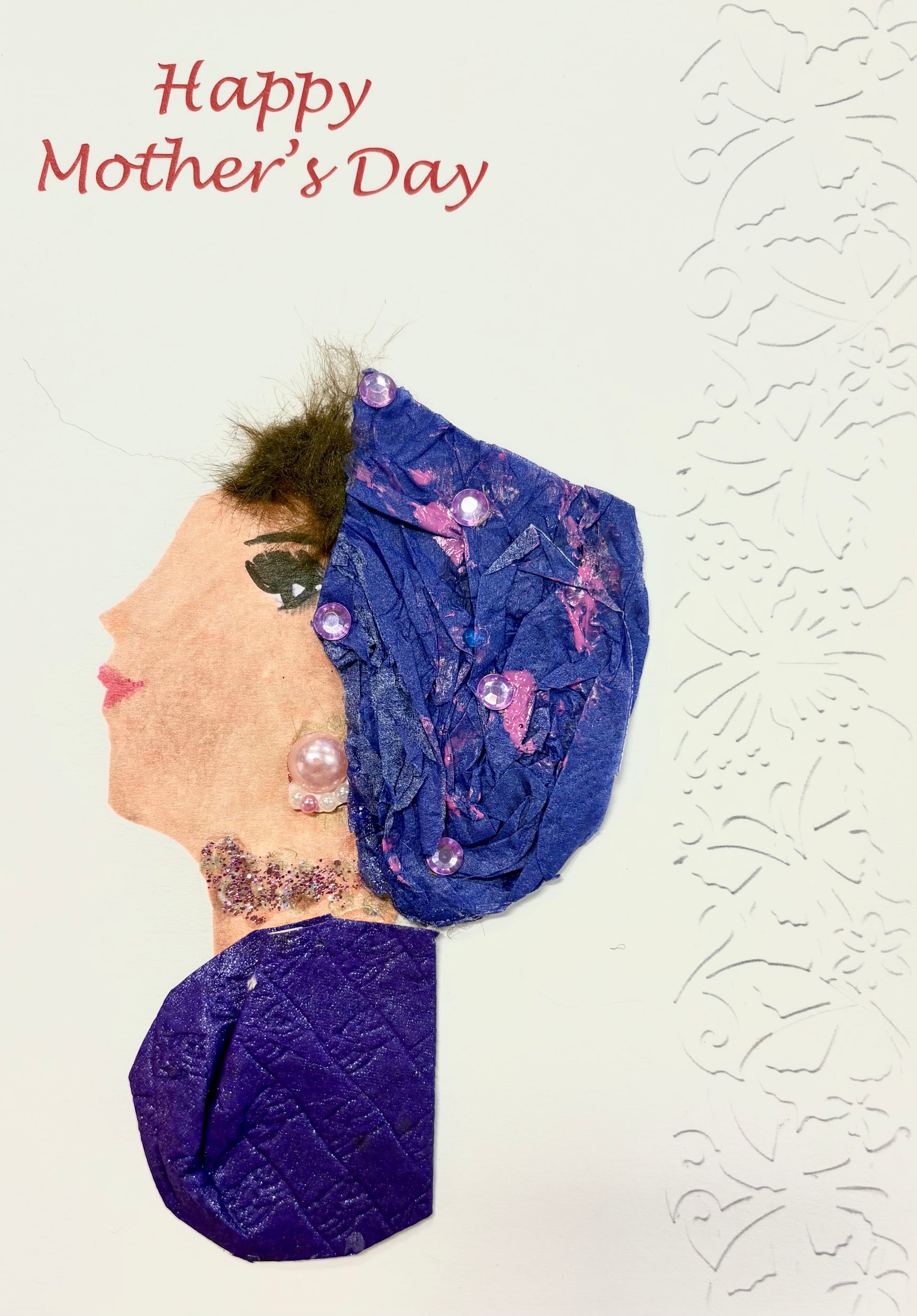 A woman wears a deep purple hat featuring pink splotches and little gems. She wears a deep purple blouse and a baby pink pearl earring. Happy Mother's Day is written in the top left corner in red font.